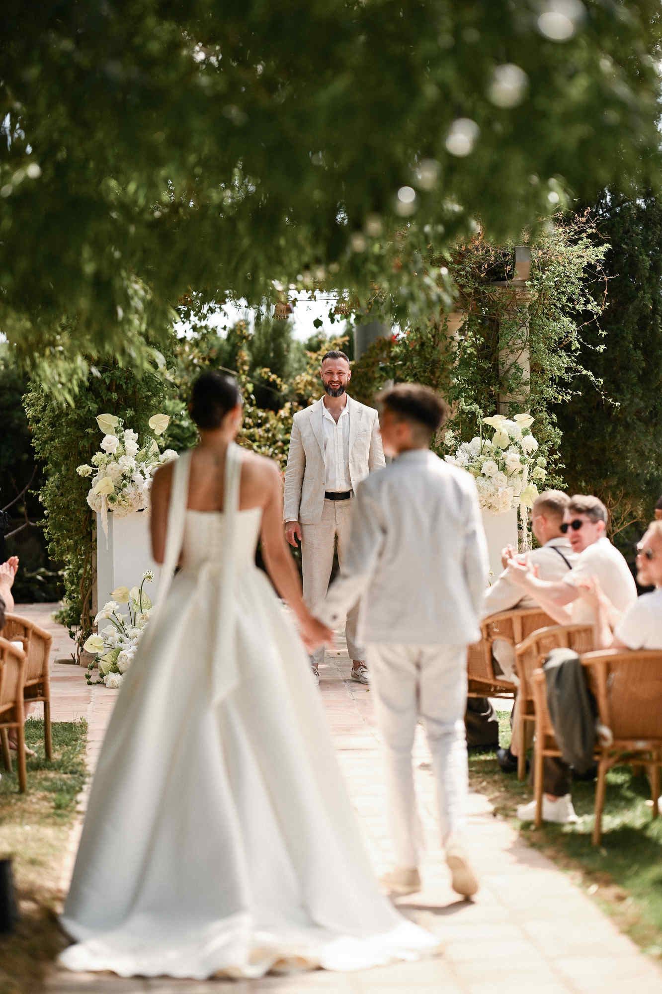 Bride walking down the aisle towards the groom during an outdoor garden wedding ceremony at Villa Paula in Valencia.
