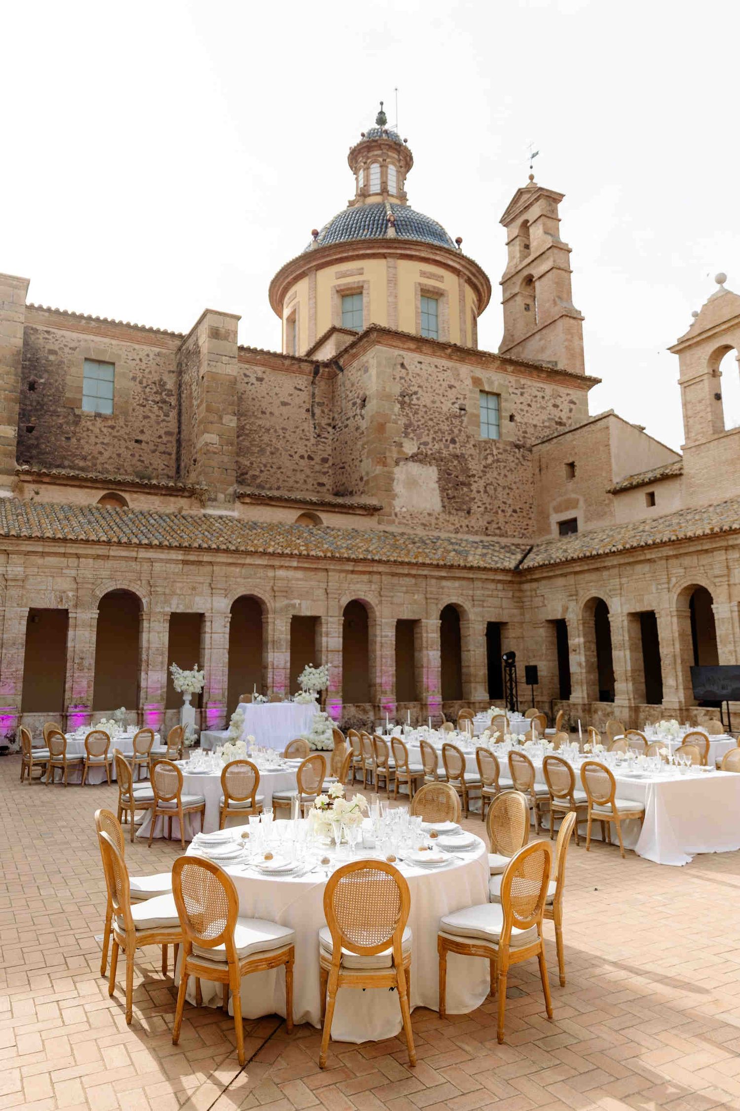 Guests dining at a cross-shaped table layout during an outdoor wedding reception in a historic cartuja monastery courtyard.