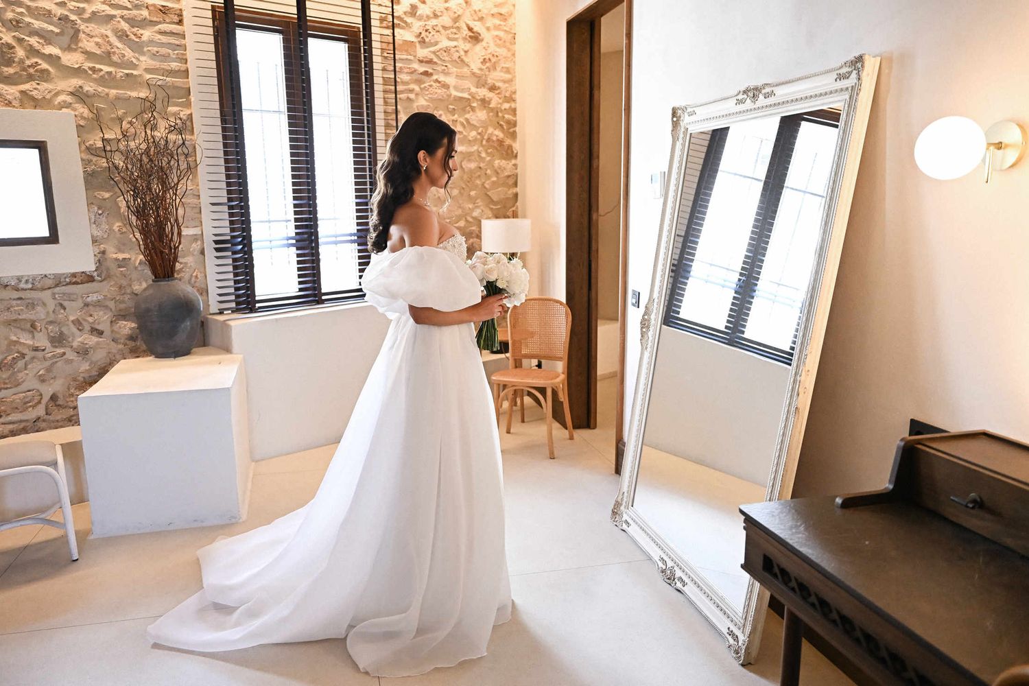 Bride admiring her off-the-shoulder wedding dress in a vintage floor mirror at Finca del Canónigo in Valencia.