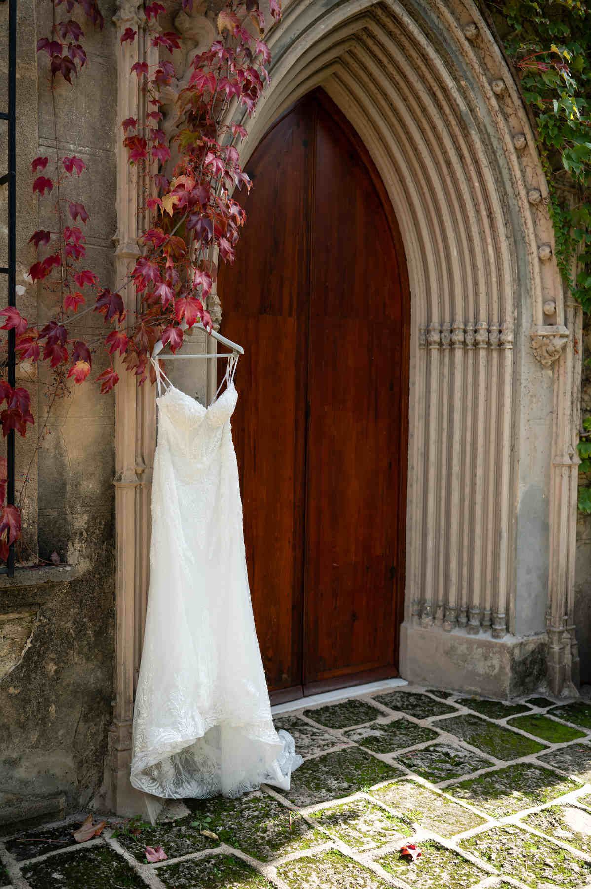 Lace wedding dress hanging on a wooden door inside a gothic stone arch with red autumn ivy at Casa Santonja.
