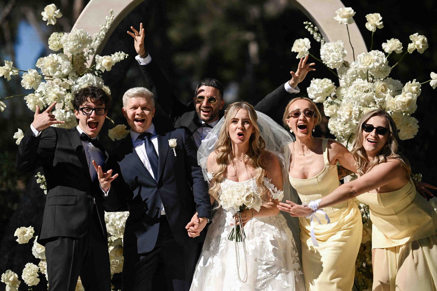 Happy bride, groom, and wedding party posing and cheering together in front of a floral arch after a wedding ceremony in finca el senyoret