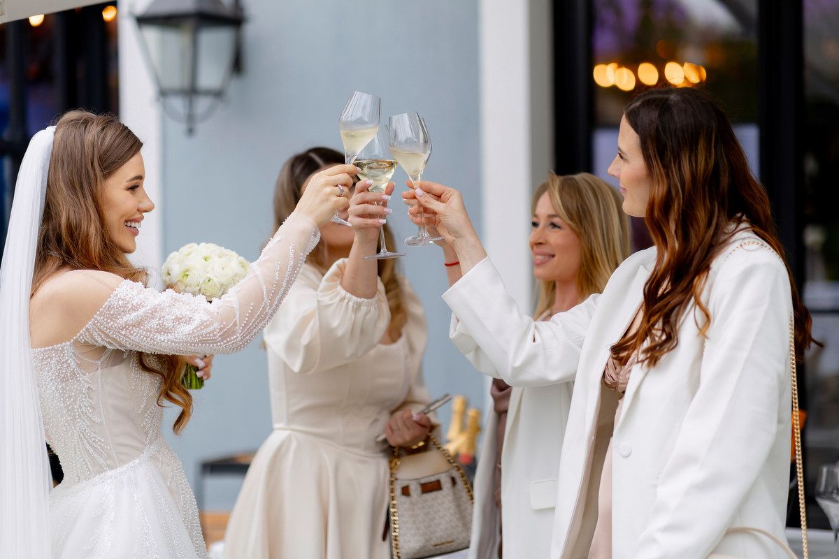 A bride in a beaded long-sleeve dress toasts with champagne glasses alongside her friends at an outdoor Alicante celebration.