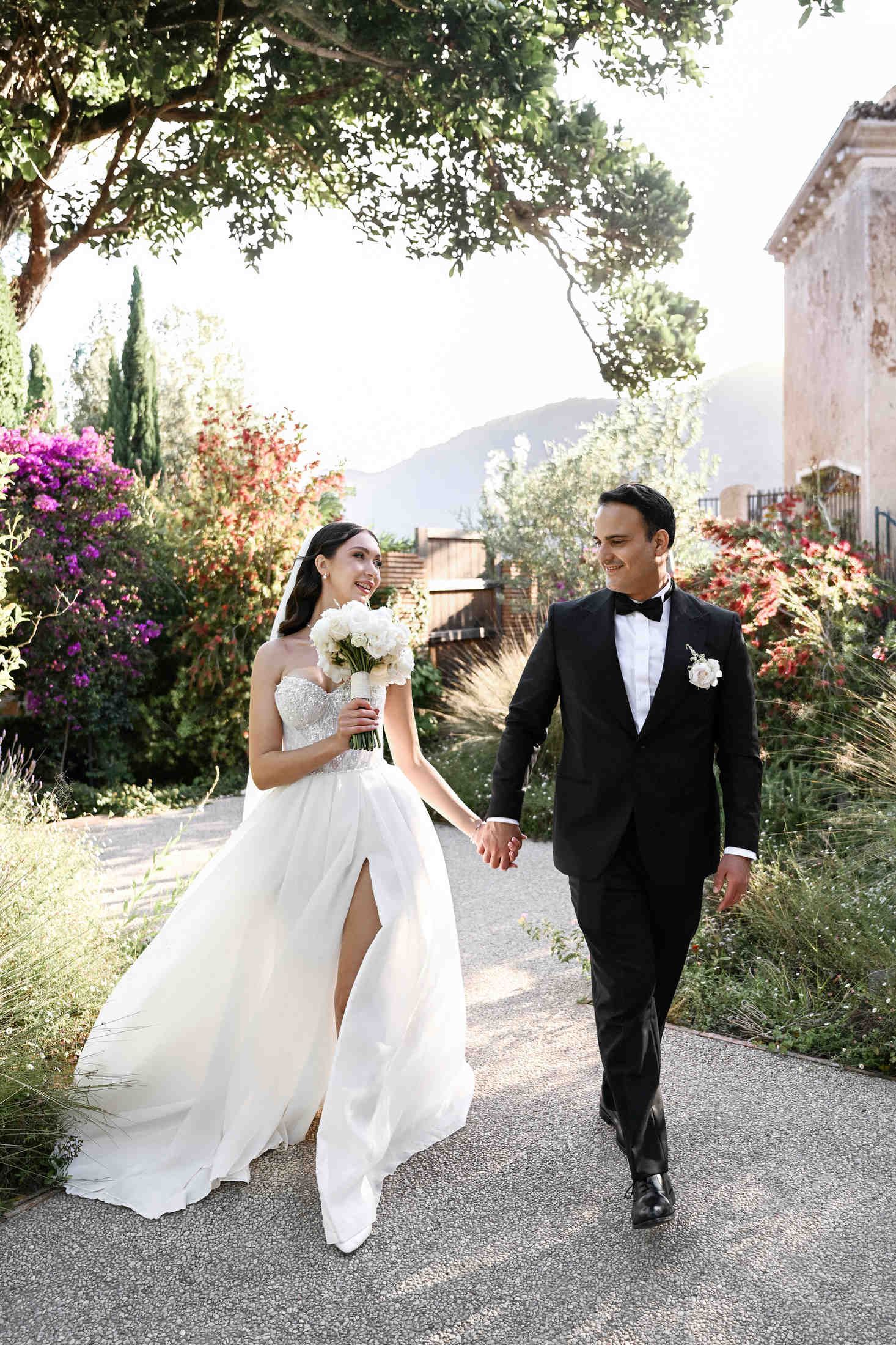 Bride and groom walking hand in hand through a lush green garden at their outdoor destination wedding in finca del canonigo