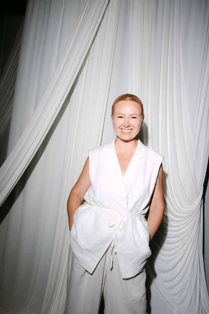 Wedding planner in Benidorm Olga Prudko, stands under a white archway in a white suite and smile.