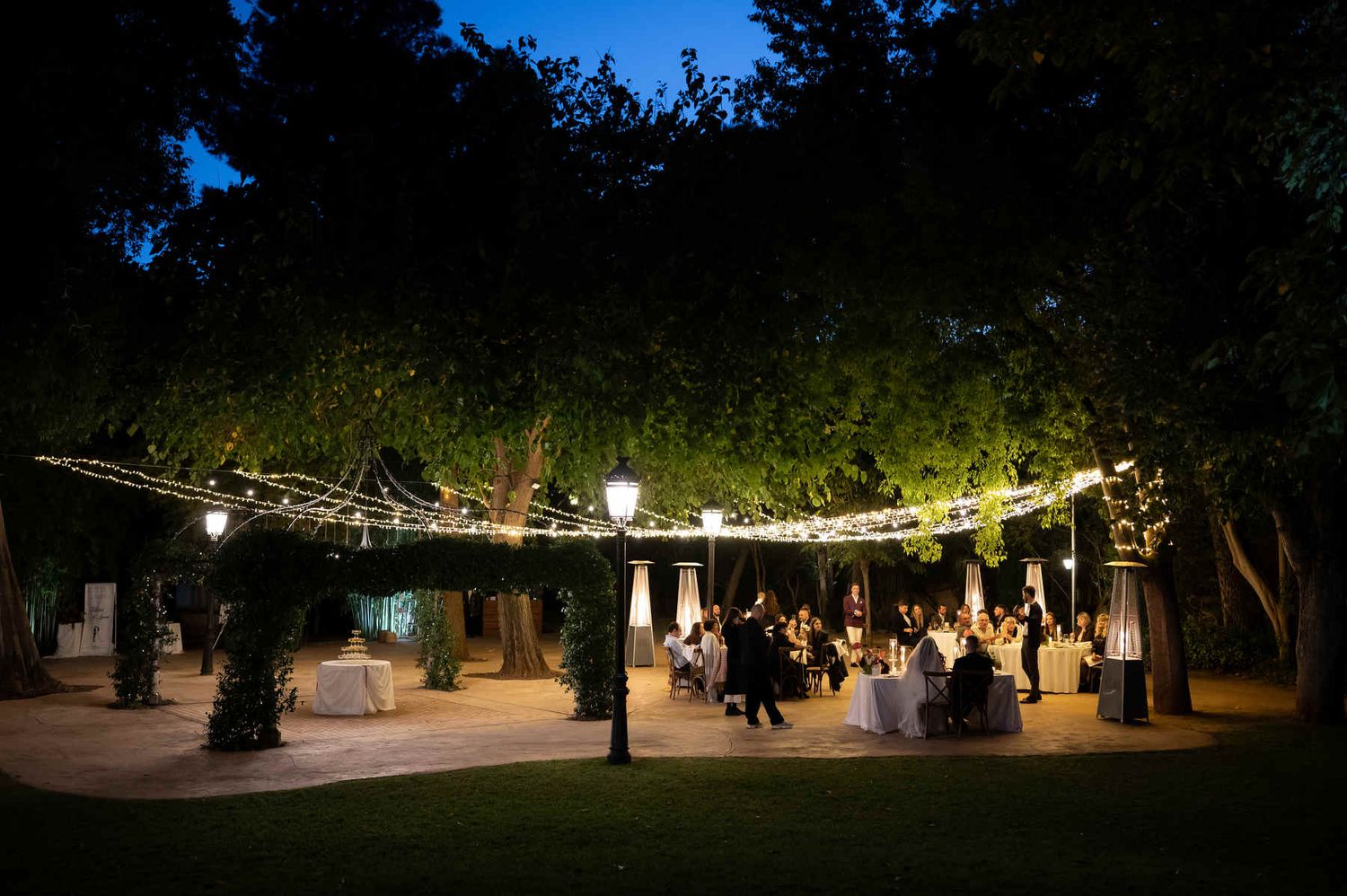 Scenic view of the outdoor evening wedding banquet illuminated by string lights in the gardens of Casa Santonja