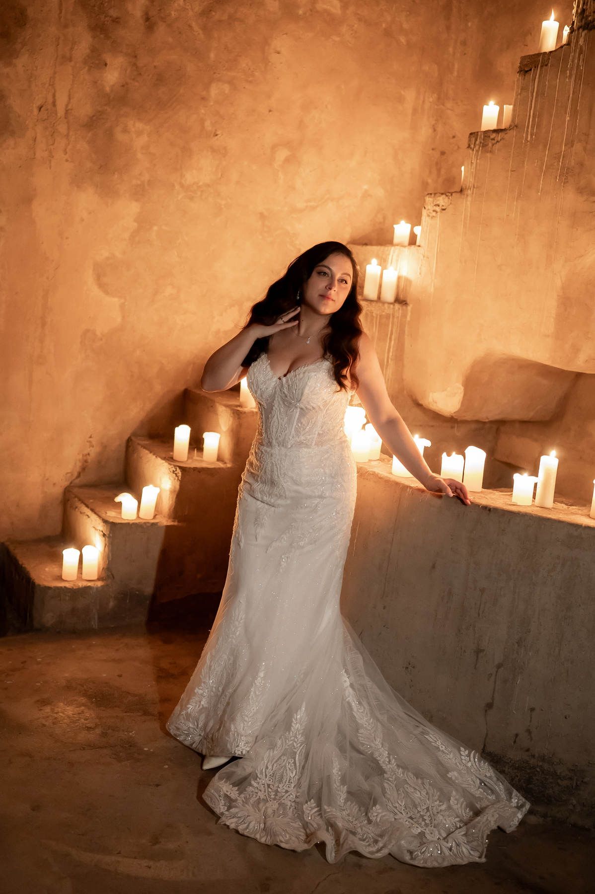 Bride in a fitted lace gown leaning against a stone wall surrounded by warm candlelight at Casa Santonja estate.