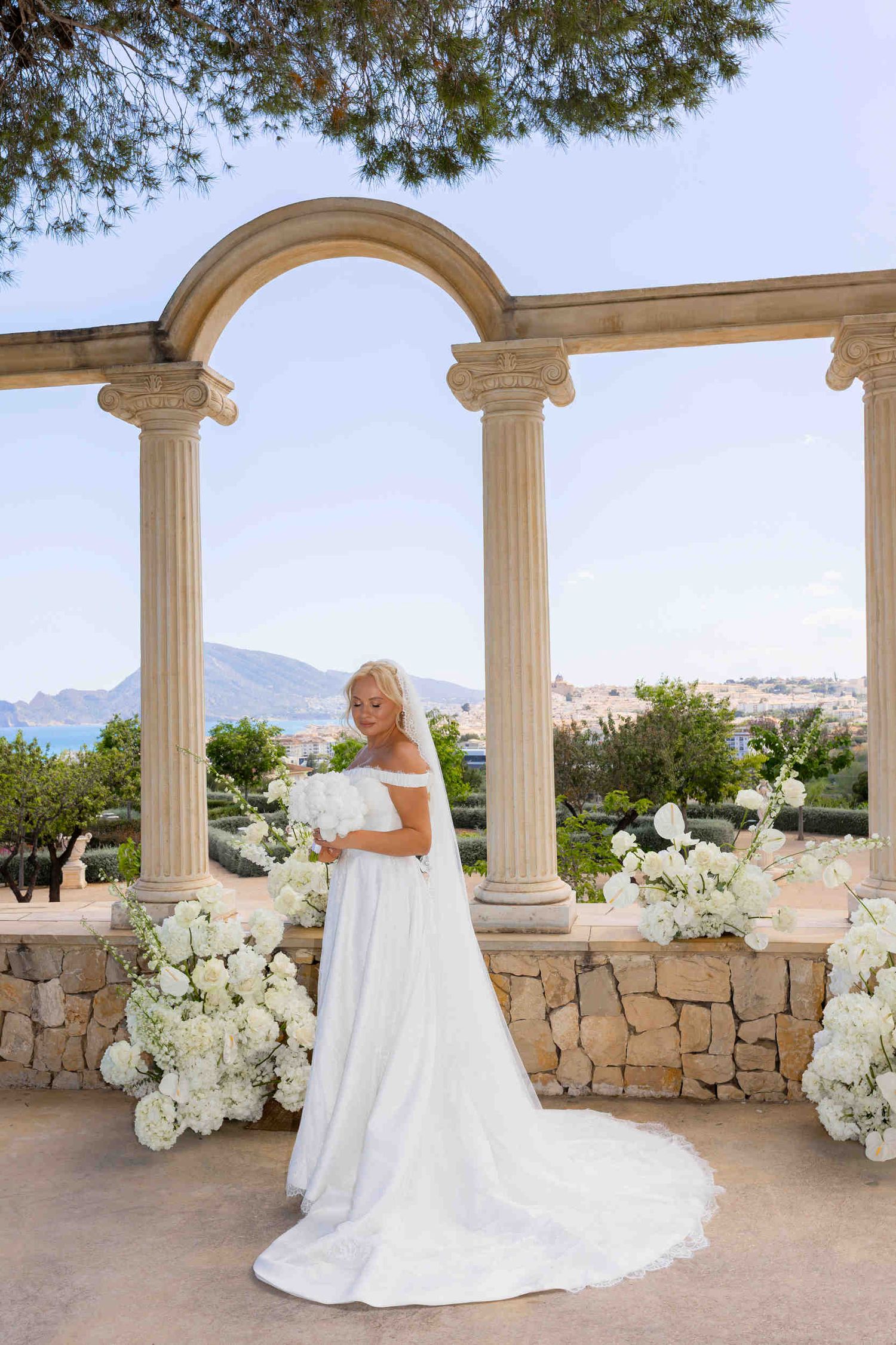 Bride standing on a beautiful stone terrace with pillars and white flowers, overlooking the sea and mountains in Altea.