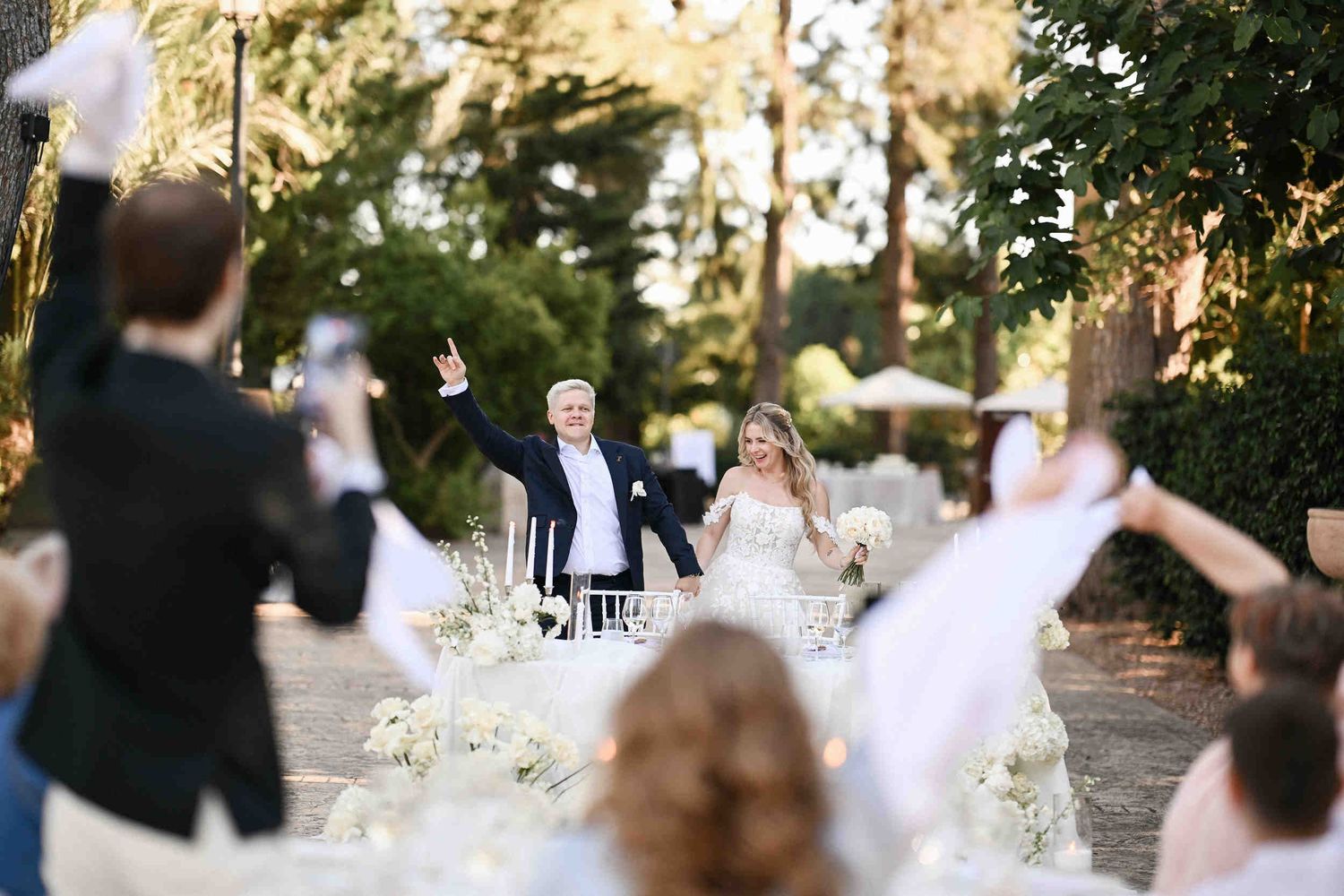 Cheering newlyweds making their grand entrance to an outdoor wedding dinner in Benidorm as guests wave white napkins.