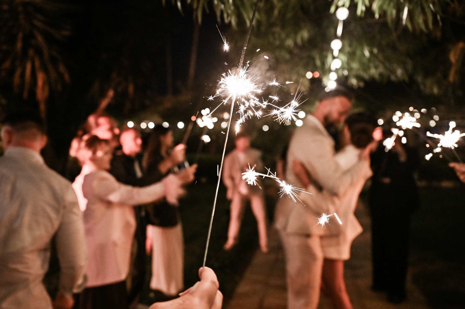 Close-up of burning sparklers with the newlywed couple romantically kissing in the background during their Valencia wedding night.