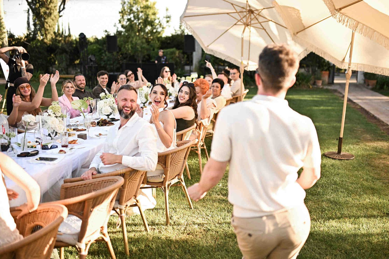 Best man running enthusiastically towards the bride and laughing guests during a fun outdoor wedding dinner.