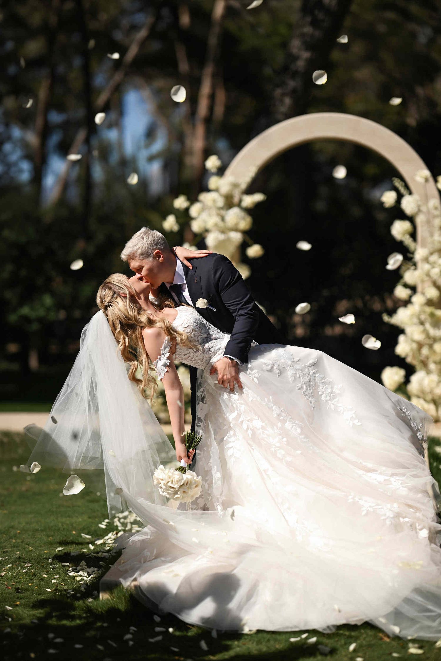 Groom dipping his bride for a kiss under falling white petals at an outdoor event styled by a Benidorm wedding planner.