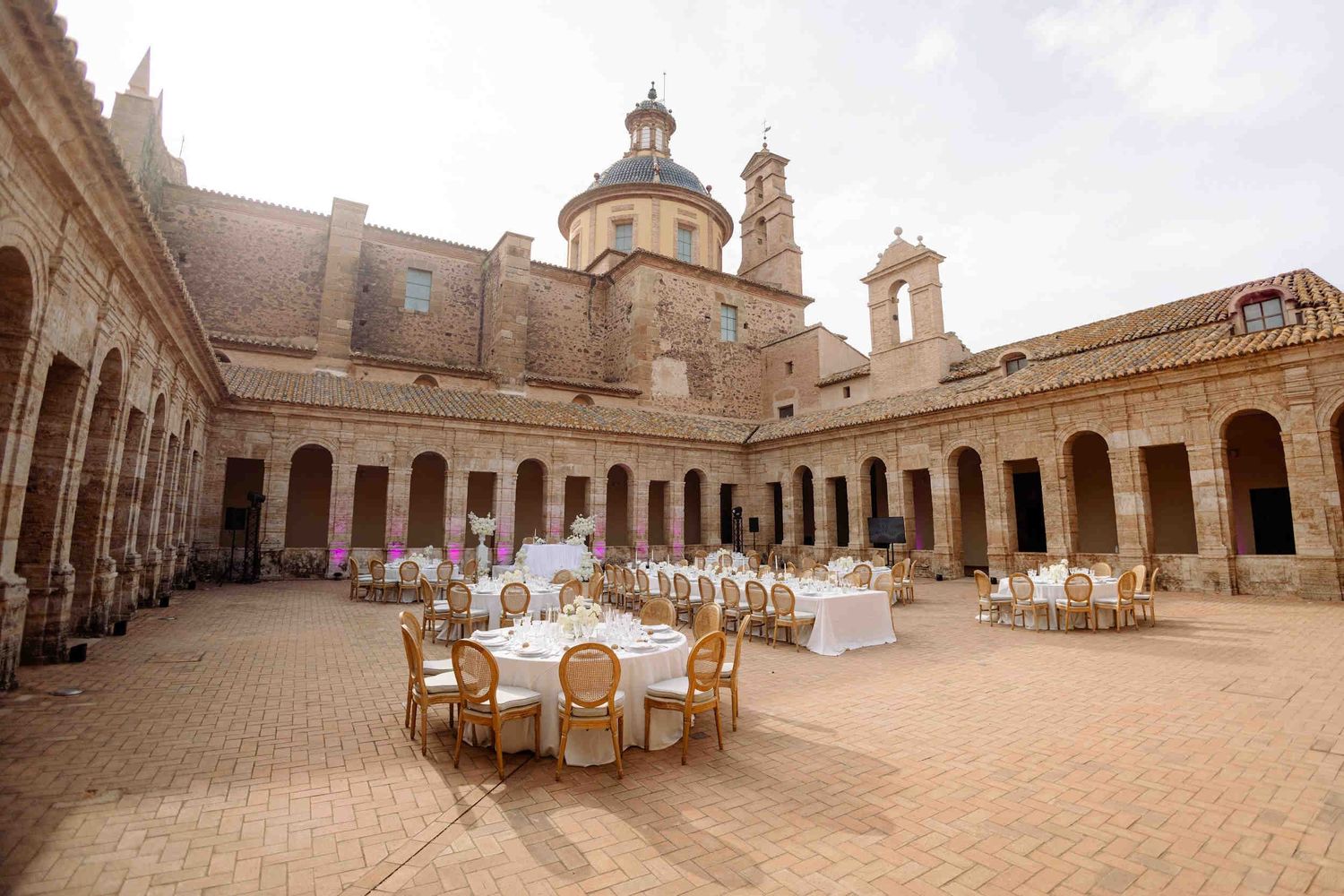 Round dinner tables set for a wedding reception inside the historic stone cloister of La Cartuja de Ara Christi.