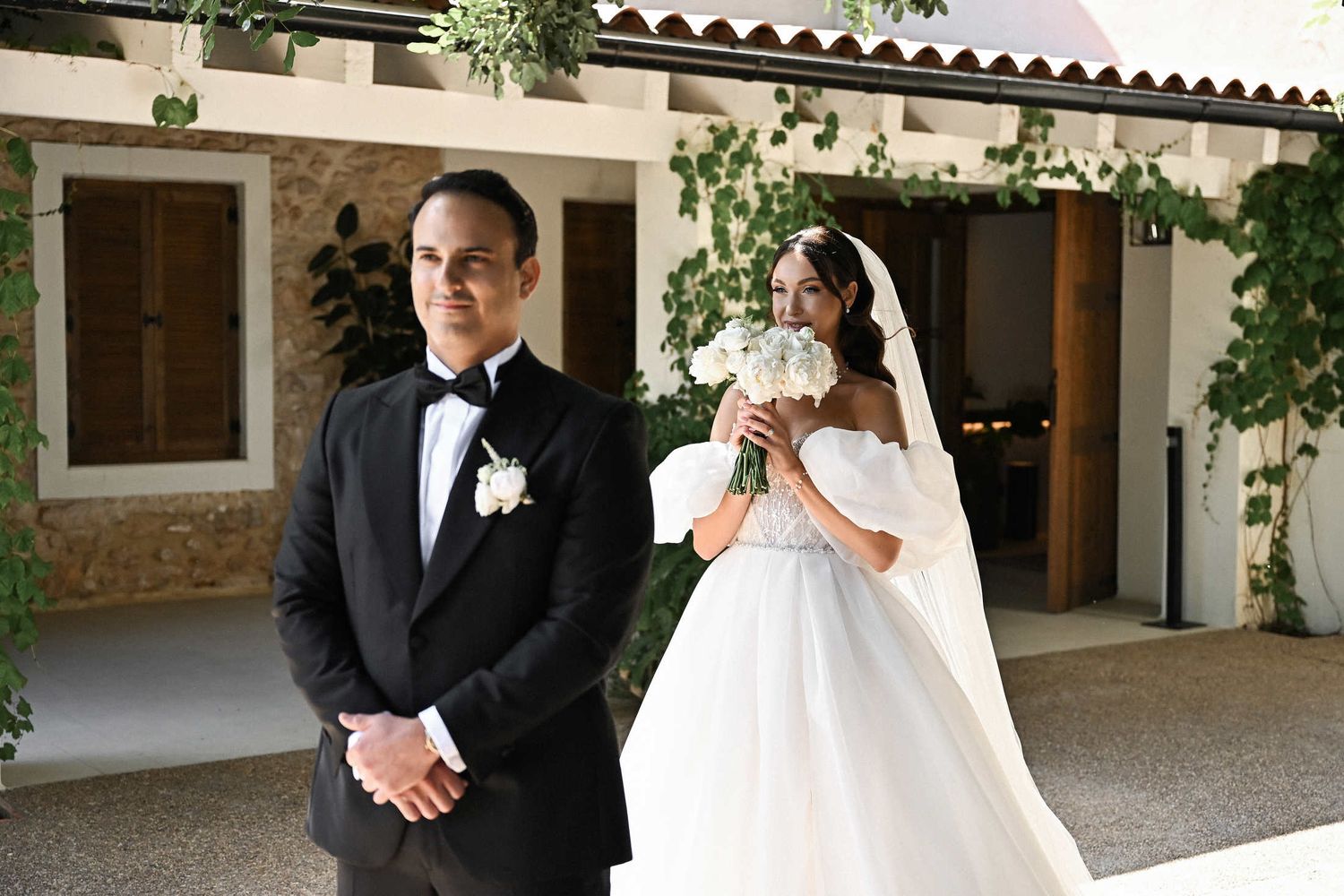 Groom waits for bride holding a white bouquet during their first look at a historic finca destination wedding in Valencia.
