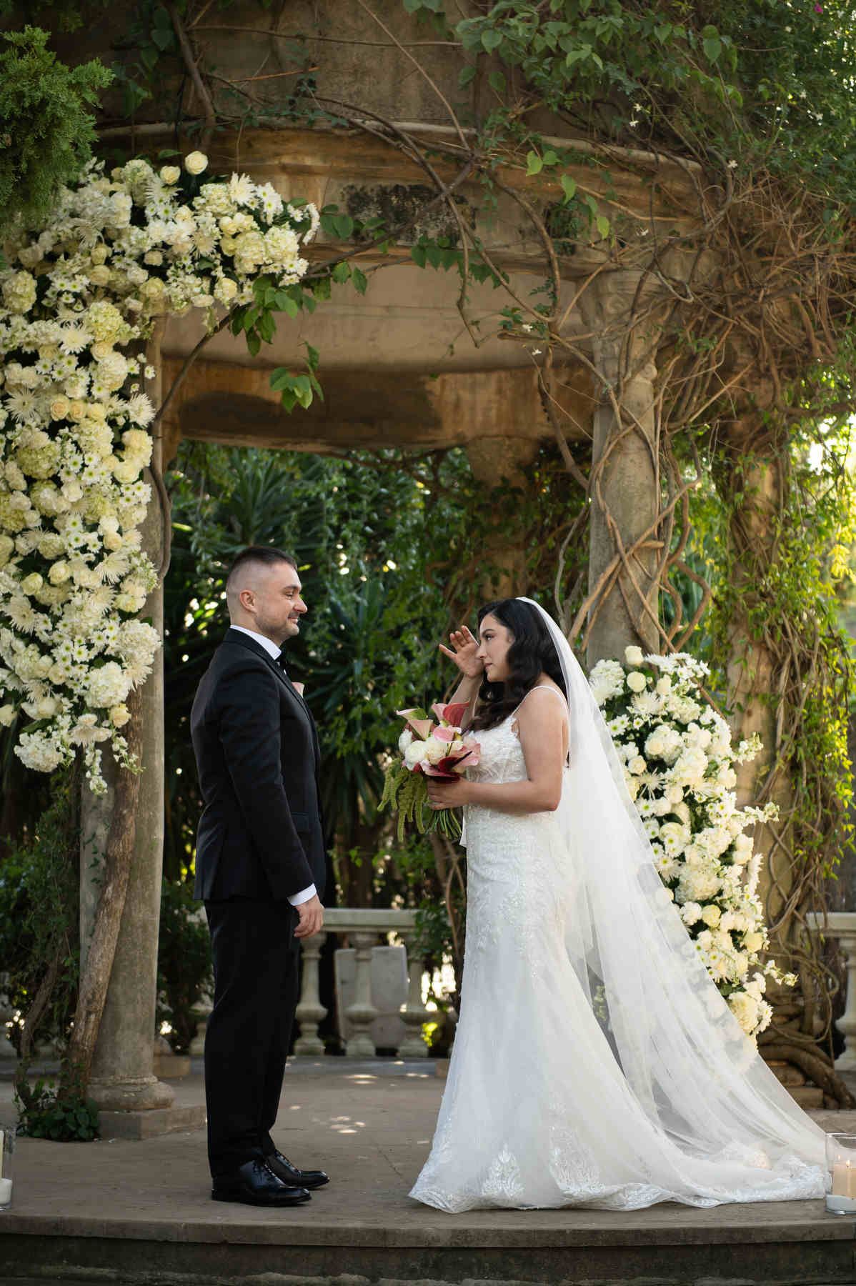Emotional bride wiping a tear during the wedding ceremony under a floral gazebo at Casa Santonja