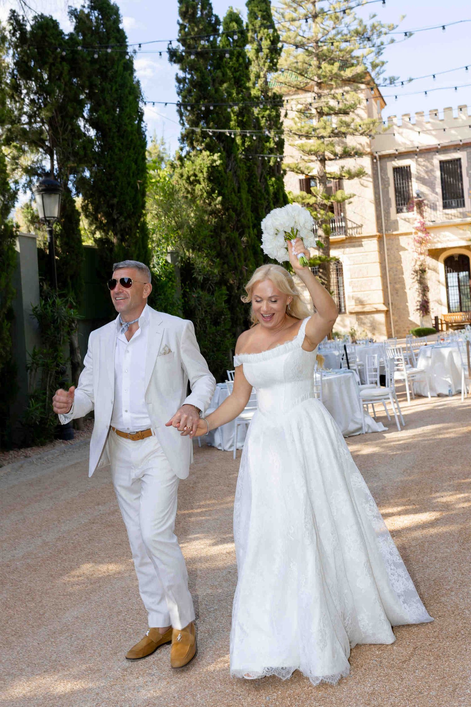 Joyful bride and groom holding hands and entering their outdoor wedding reception at Finca Marques de Montemolar in Altea.