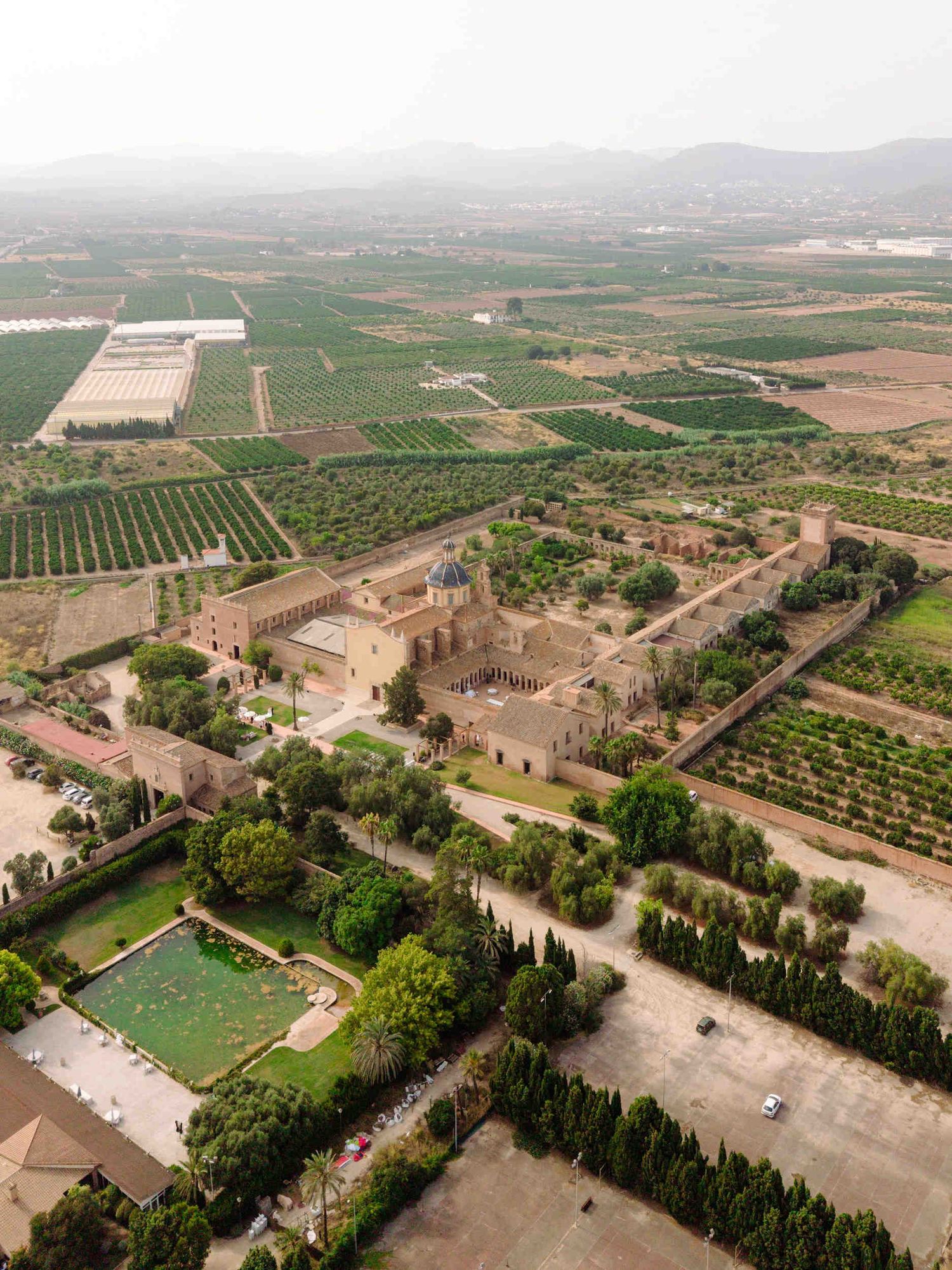 Aerial view of the historic La Cartuja de Ara Christi wedding venue near Valencia, surrounded by vast green orange groves.