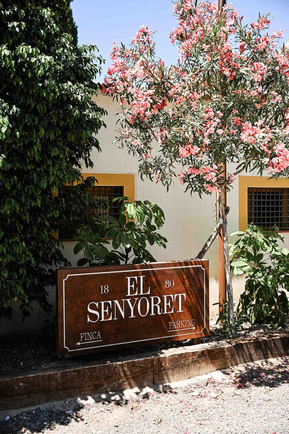 Rusty metal entrance sign for Finca El Senyoret surrounded by pink flowers at a beautiful wedding venue in benidorm.