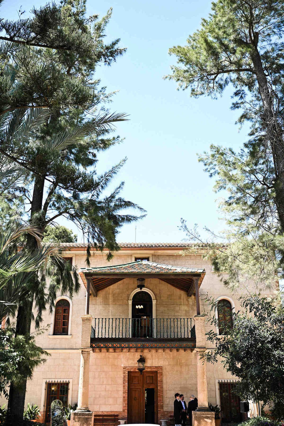 Beautiful stone facade and balcony of Finca El Senyoret surrounded by pine trees, an elegant wedding venue in Alicante.