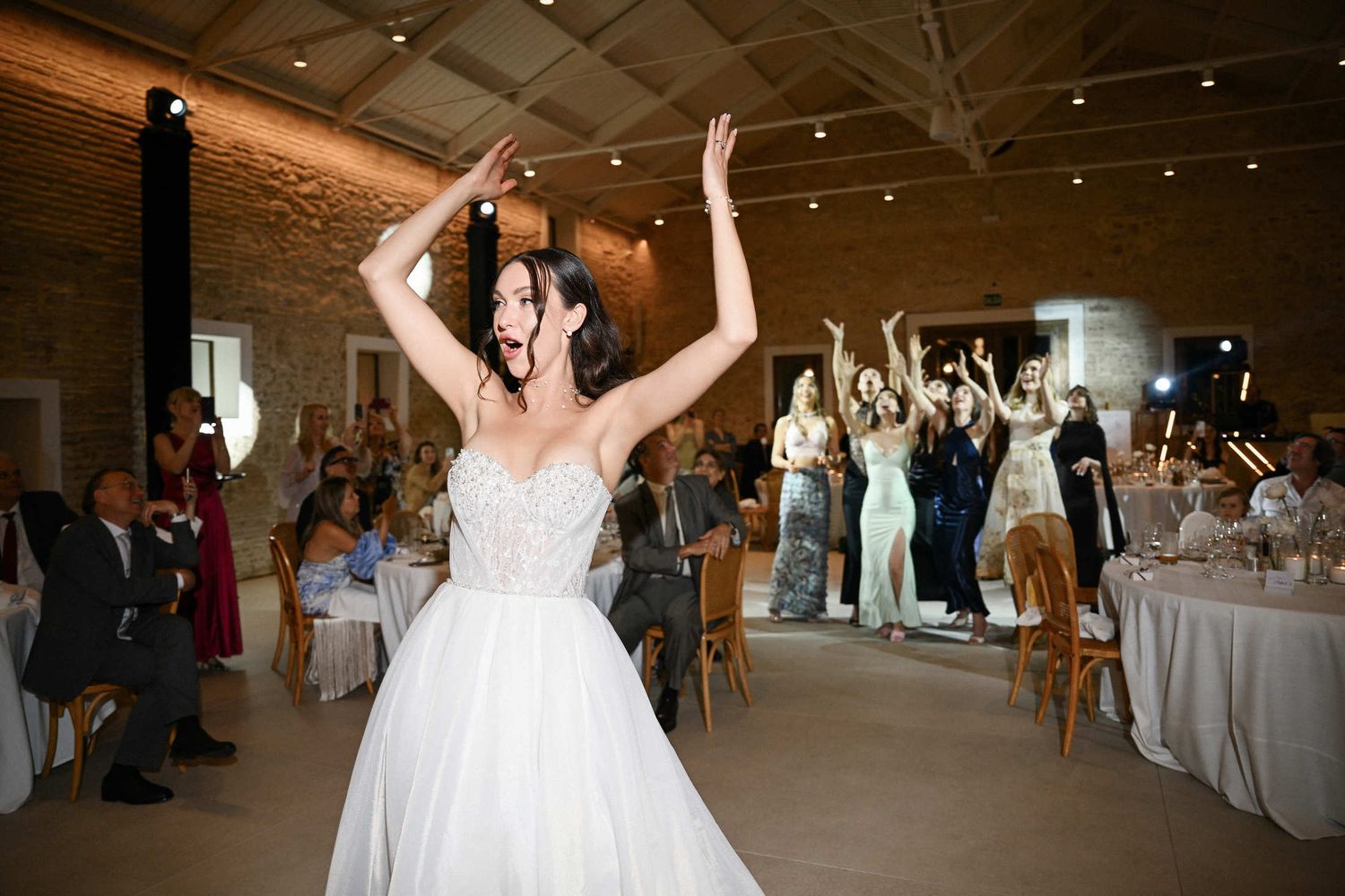 Happy bride preparing to throw her bouquet to excited guests during a fun indoor wedding reception in finca del canonigo