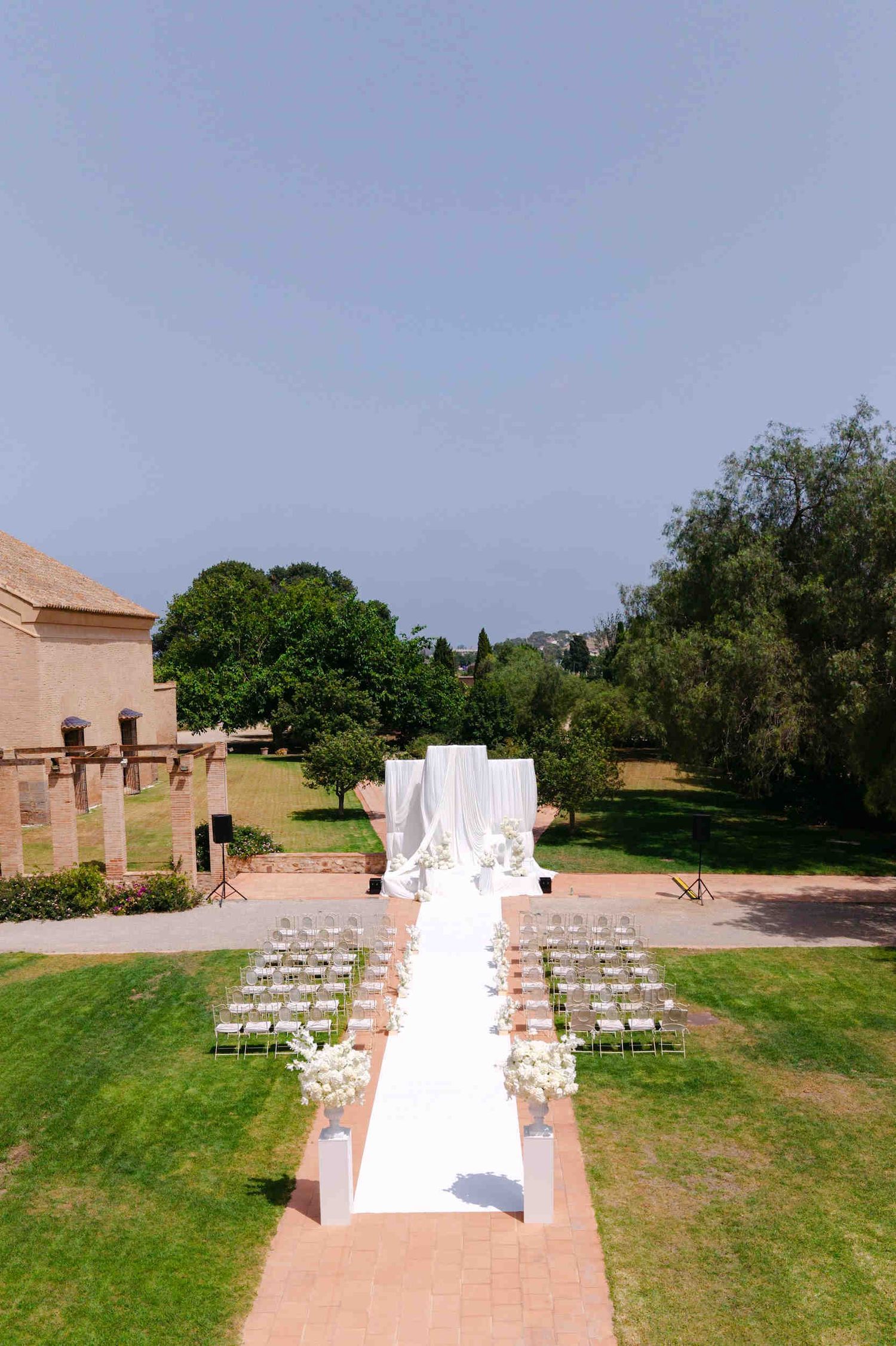 Aerial view of an outdoor wedding ceremony at La Cartuja de Ara Christi with a white draped altar on a green lawn