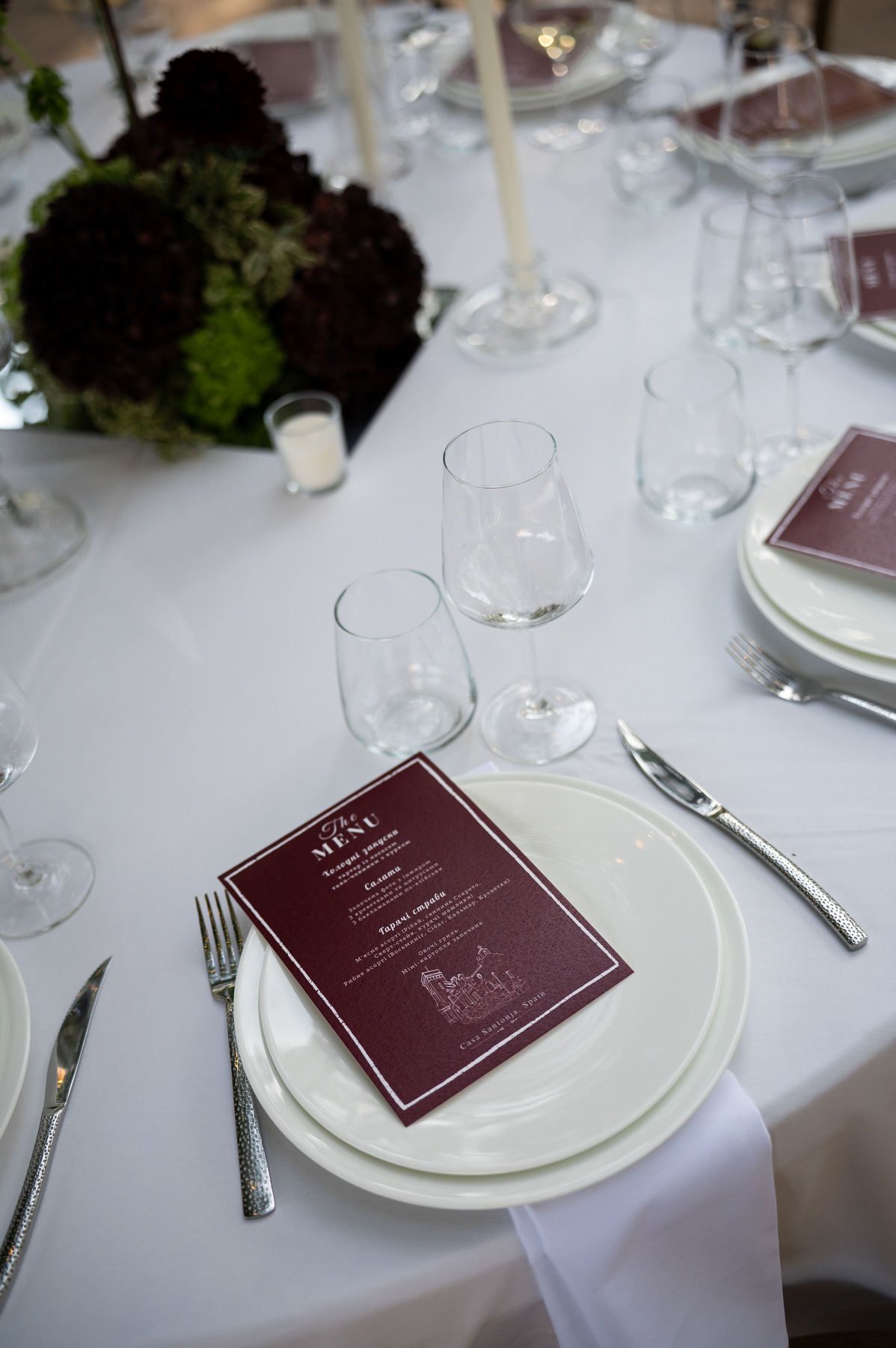 Wedding table setting with a burgundy menu, white plates and dark floral centrepieces at Casa Santonja.