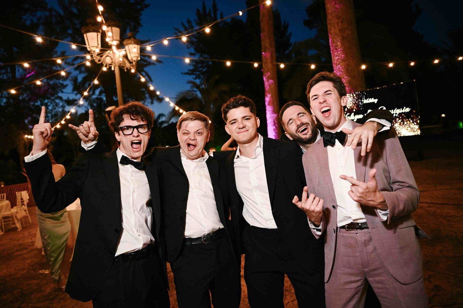 Groom and his friends making funny faces and having fun on the dance floor at a nighttime outdoor wedding reception in Spain