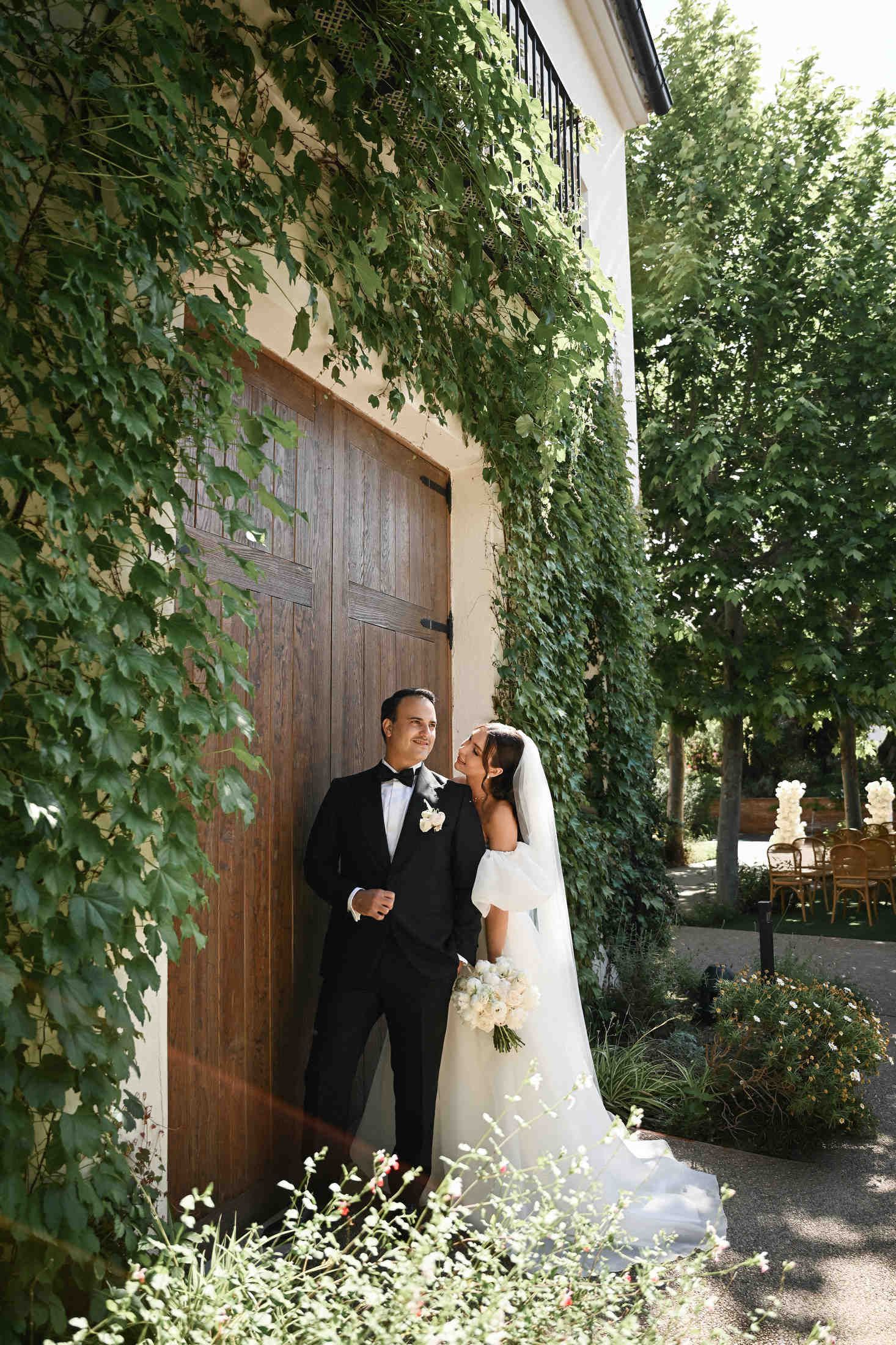 Newlyweds posing by large wooden doors and ivy-covered walls at Finca del Canónigo, planned by a Valencia wedding expert.