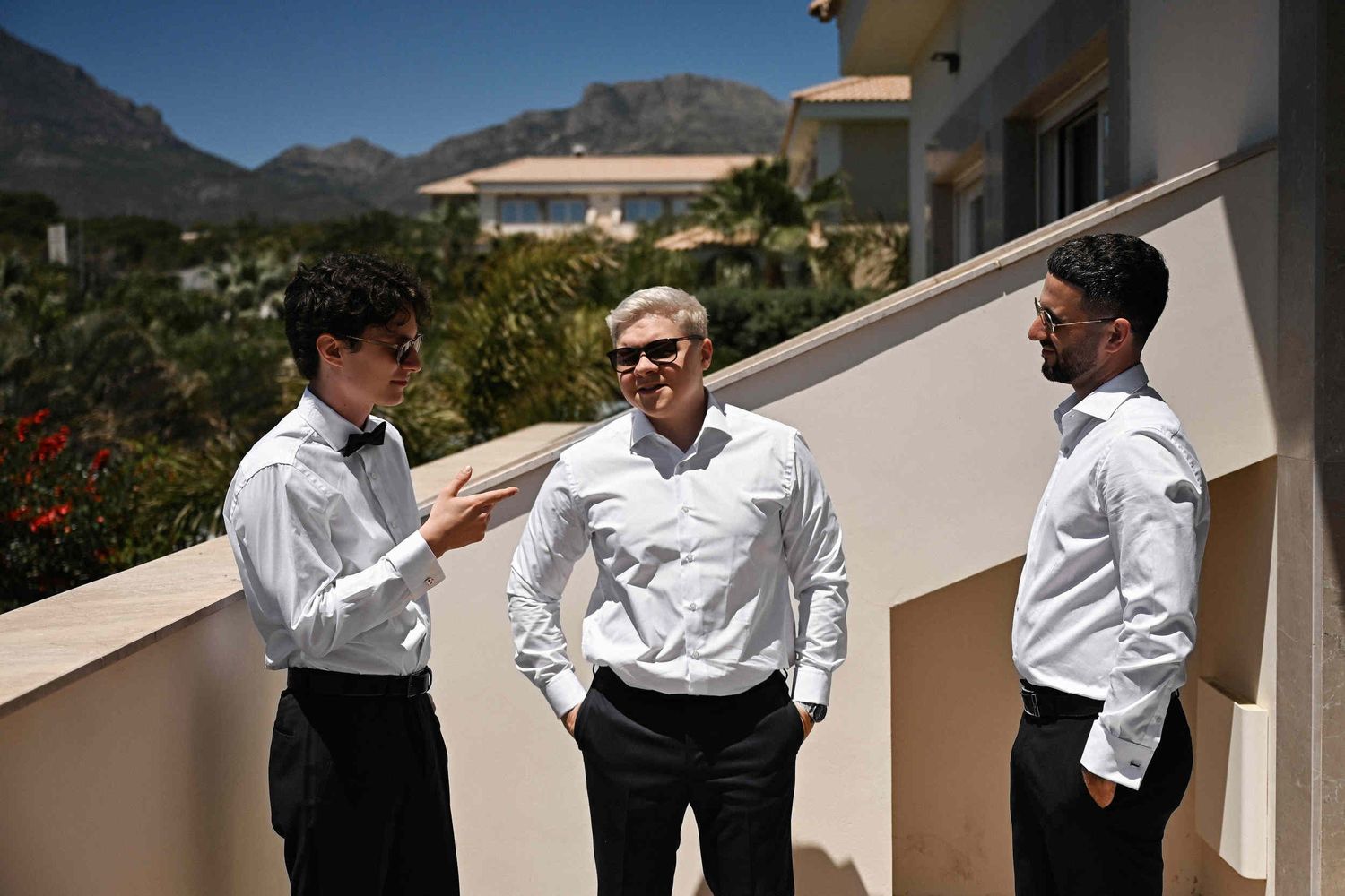 Groom and groomsmen chatting on a sunny balcony with mountain views before a destination wedding in benidorm, Spain.