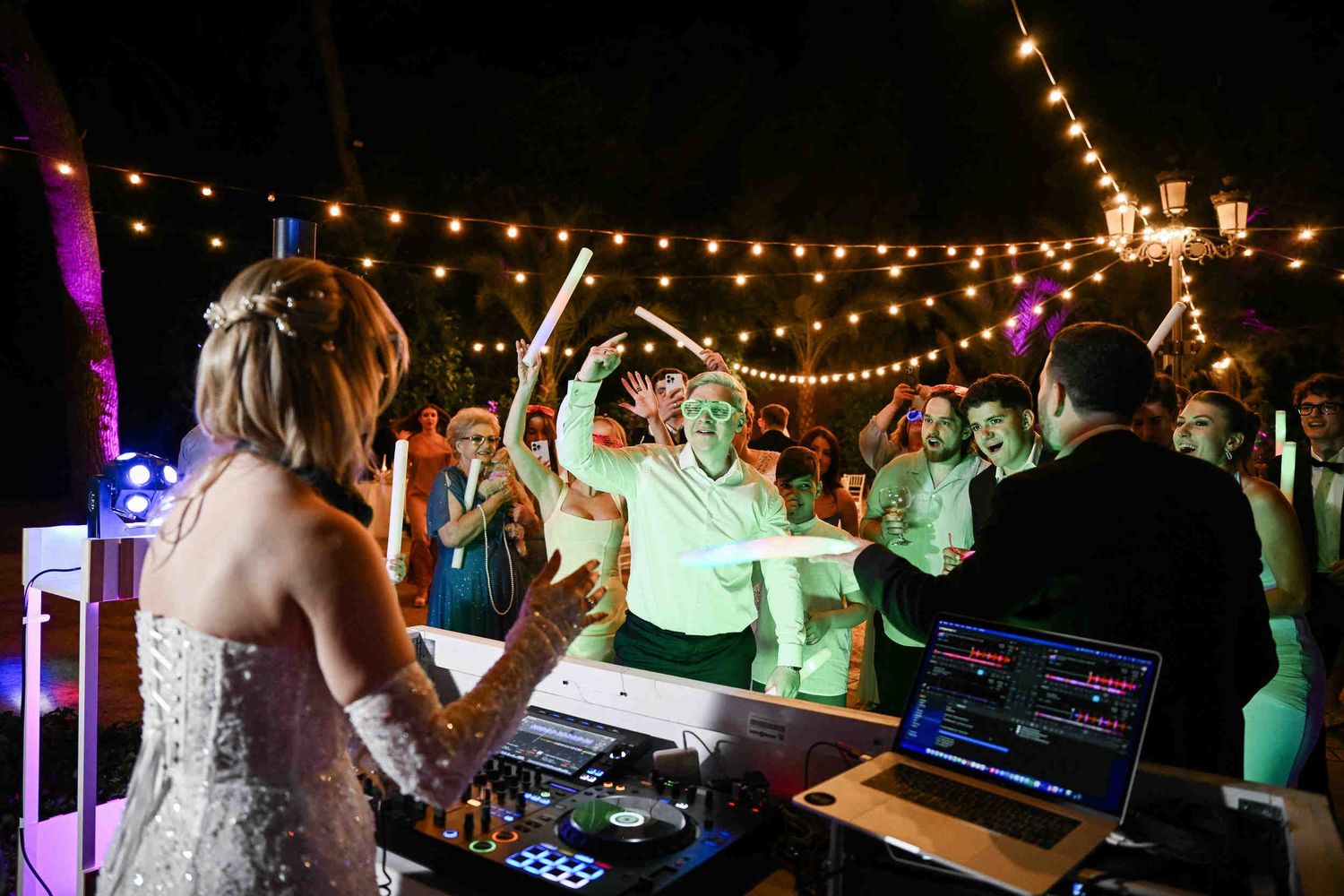 Groom in LED glasses dancing with friends holding glow sticks while the bride DJs their outdoor wedding party at Finca El Senyoret.
