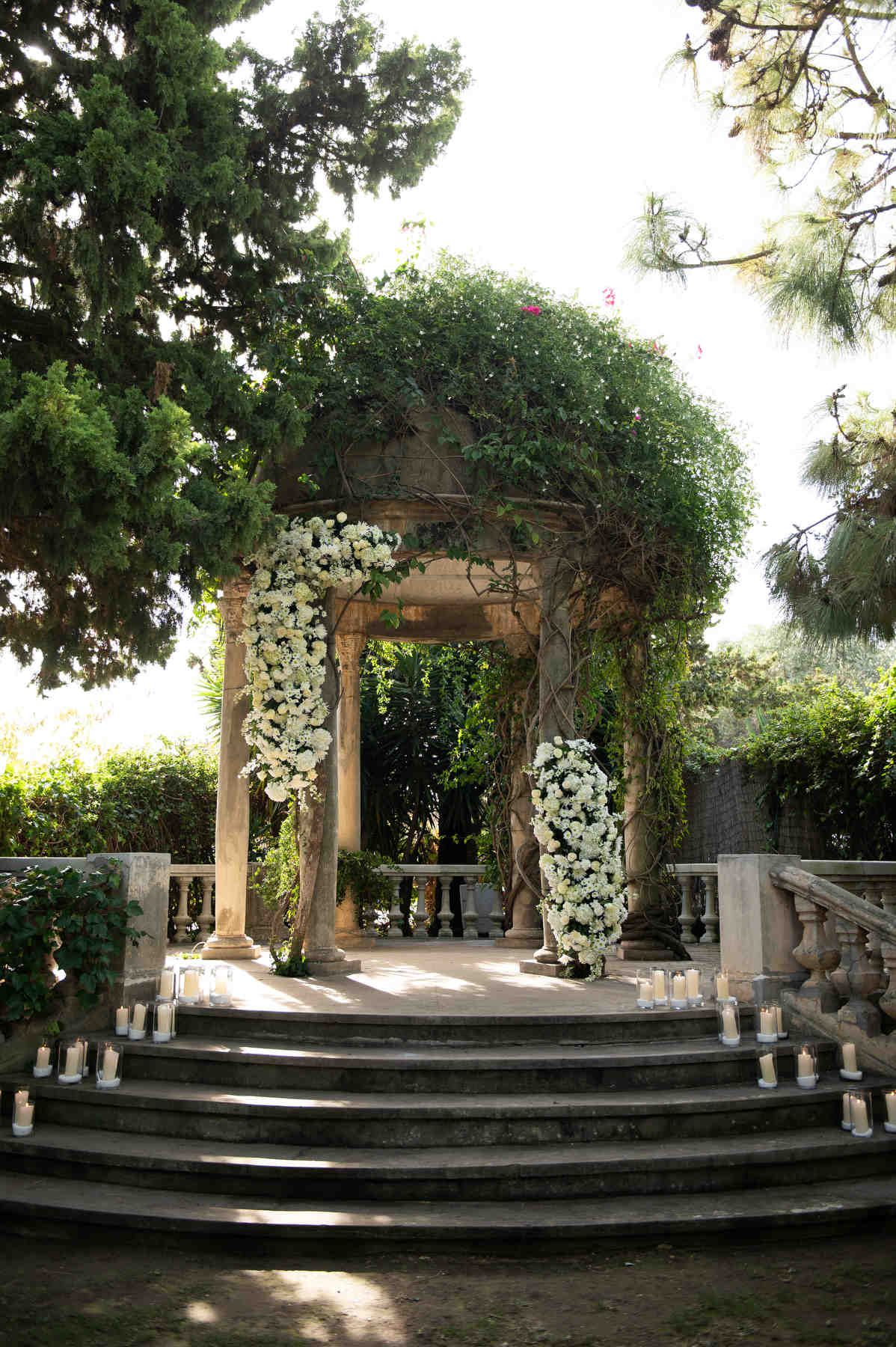 Outdoor ceremony setup at Casa Santonja near Denia, featuring a historic stone gazebo decorated with white flowers and candles.