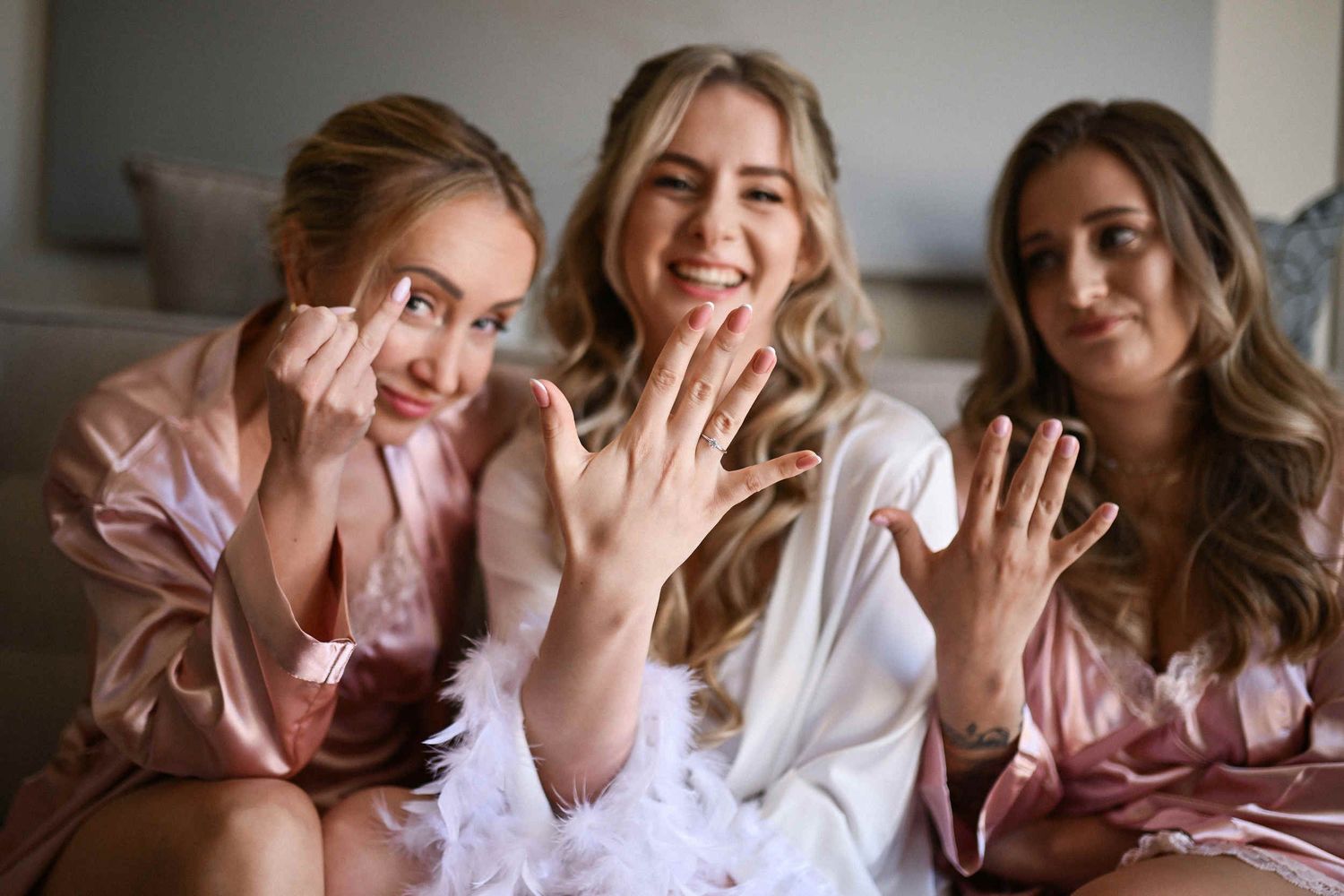 Happy bride showing off her engagement ring with smiling bridesmaids in pink robes during wedding preparations in Spain.