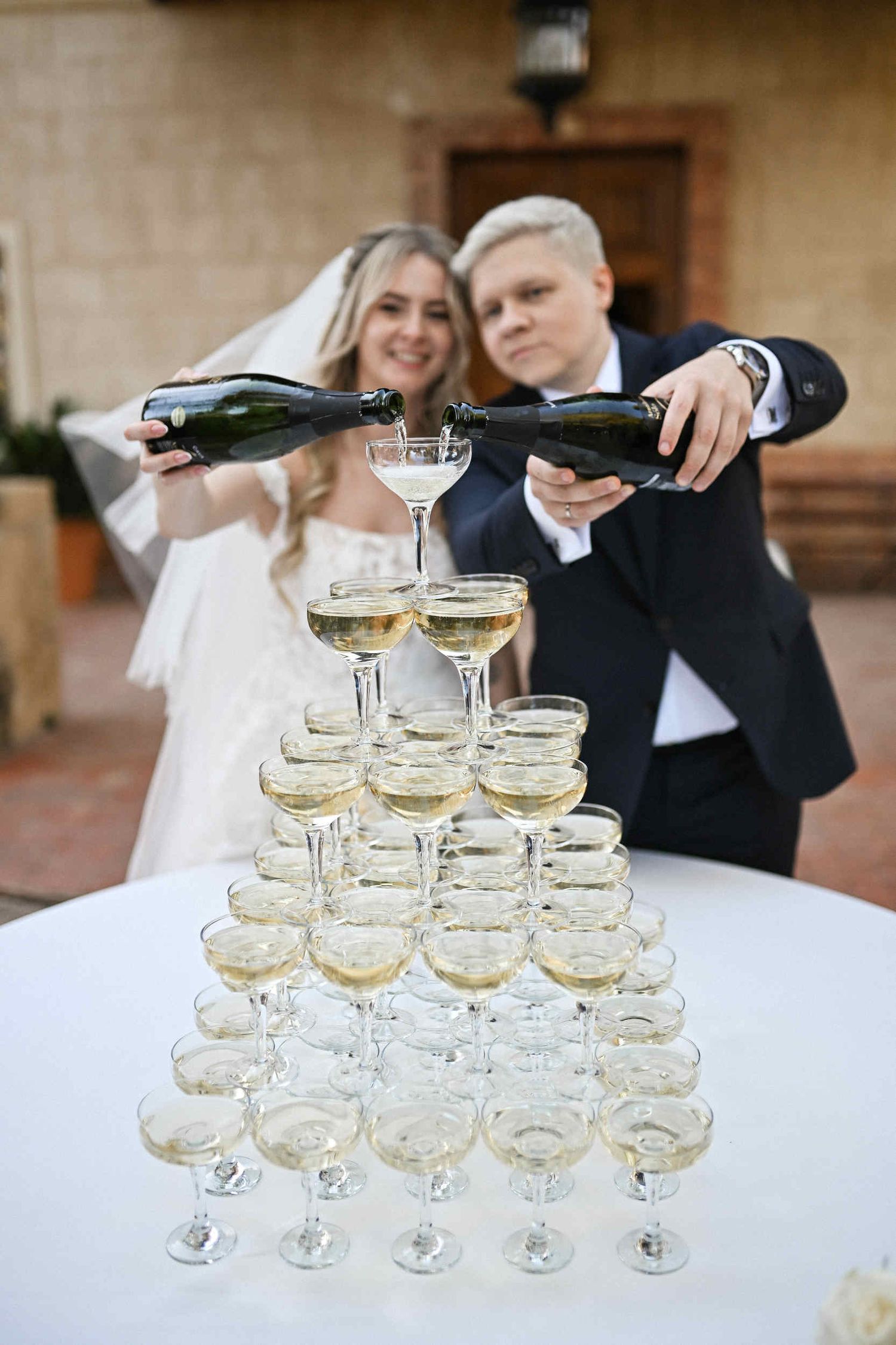 Bride and groom pouring champagne into a glass tower at an elegant outdoor wedding celebration in Benidorm.