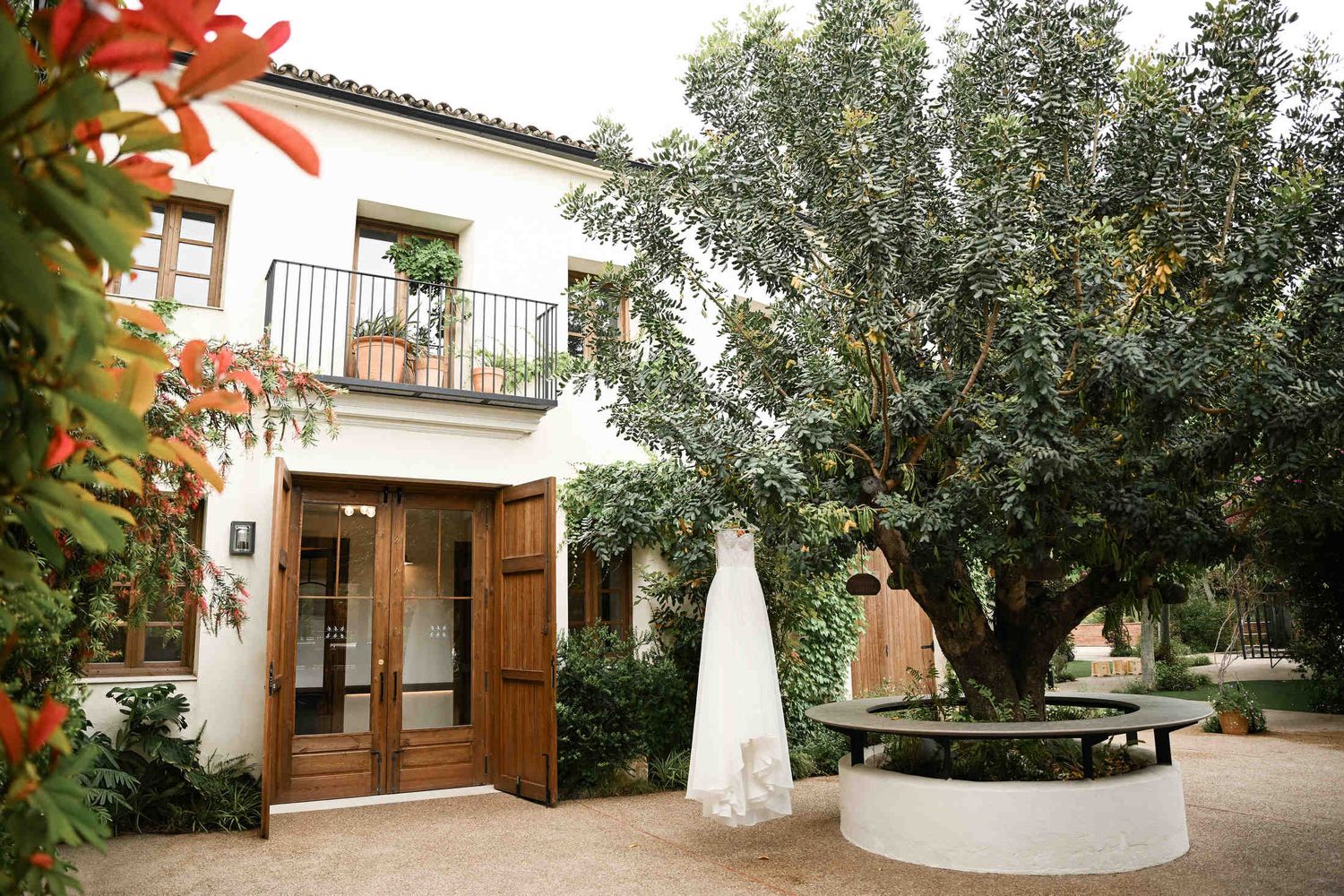 A white wedding dress hanging from a large tree in the courtyard of a historic finca before a Valencia destination wedding.