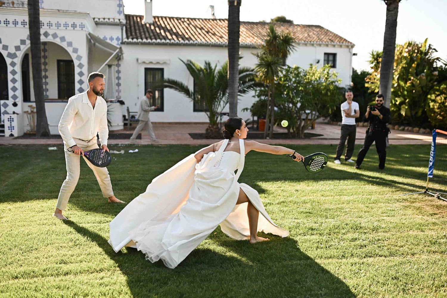Bride having fun playing padel in her wedding dress with the groom on the lawn at Villa Paula.