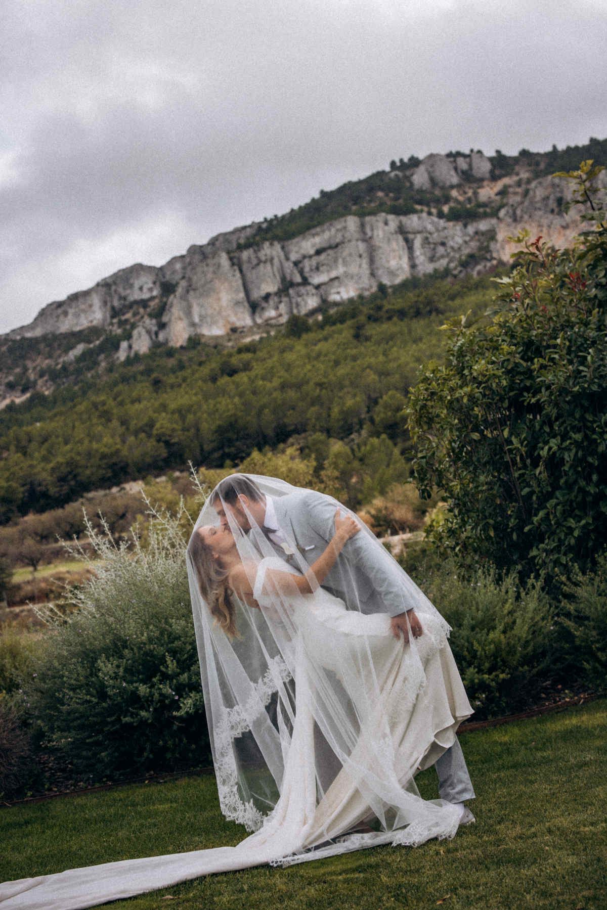 Couple kissing under the bride’s lace veil with the mountains of the Guadalest Valley behind them.