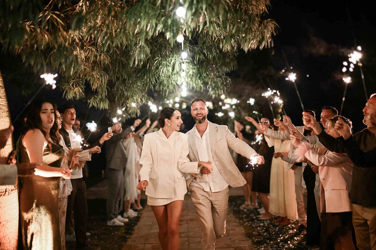 Happy bride and groom walking through a romantic wedding sparkler tunnel created by cheering guests at Villa Paula in Valencia.