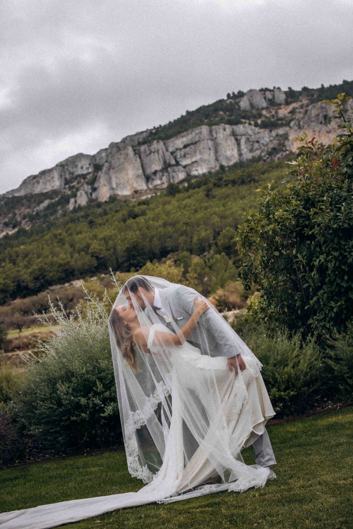 A beautiful winery wedding at Bodega Masos in the Guadalest Valley. Newlyweds kissing under a lace veil in the mountains.