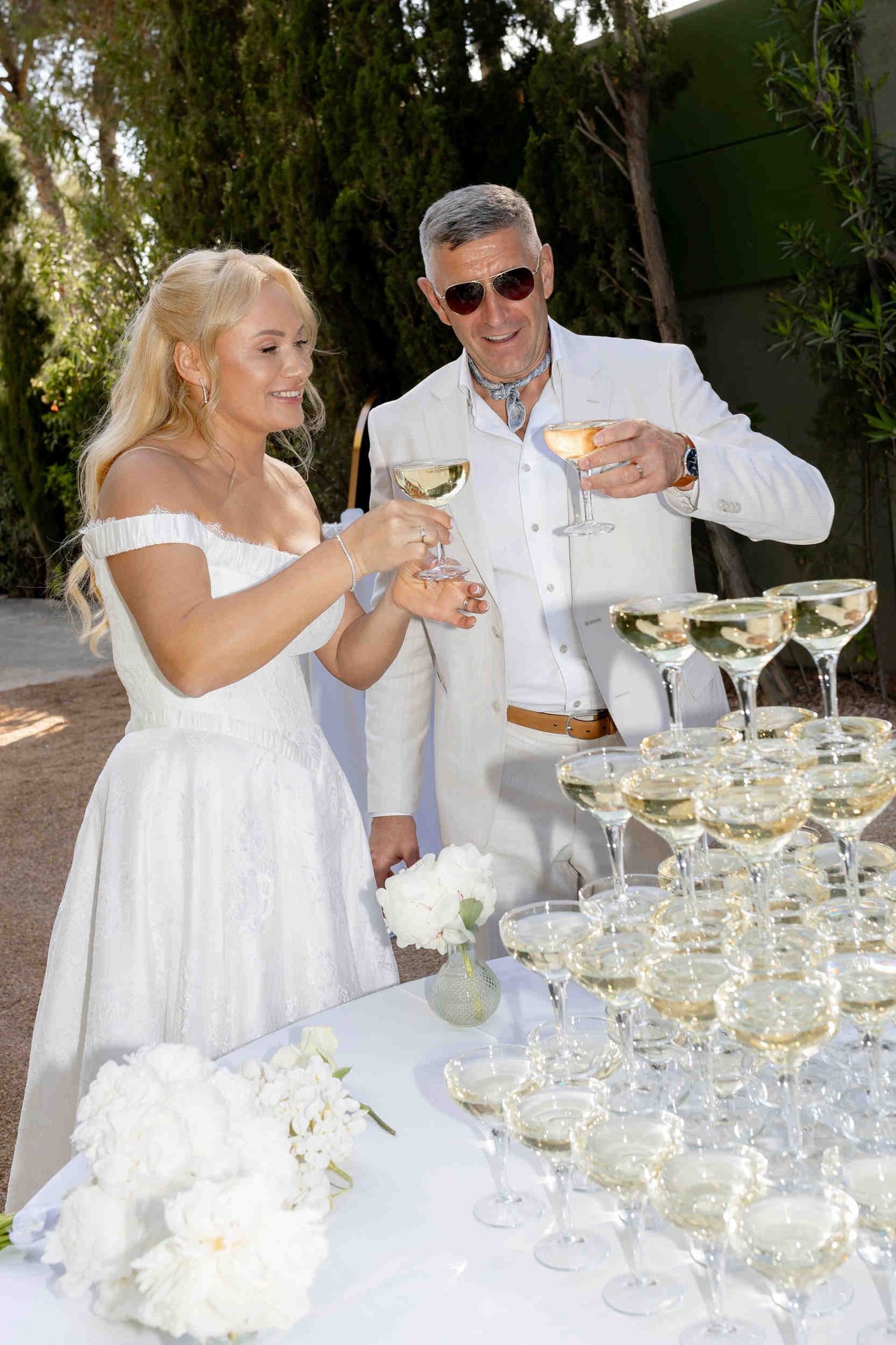 Bride and groom toasting with champagne next to a luxury champagne tower at a wedding reception in Altea.