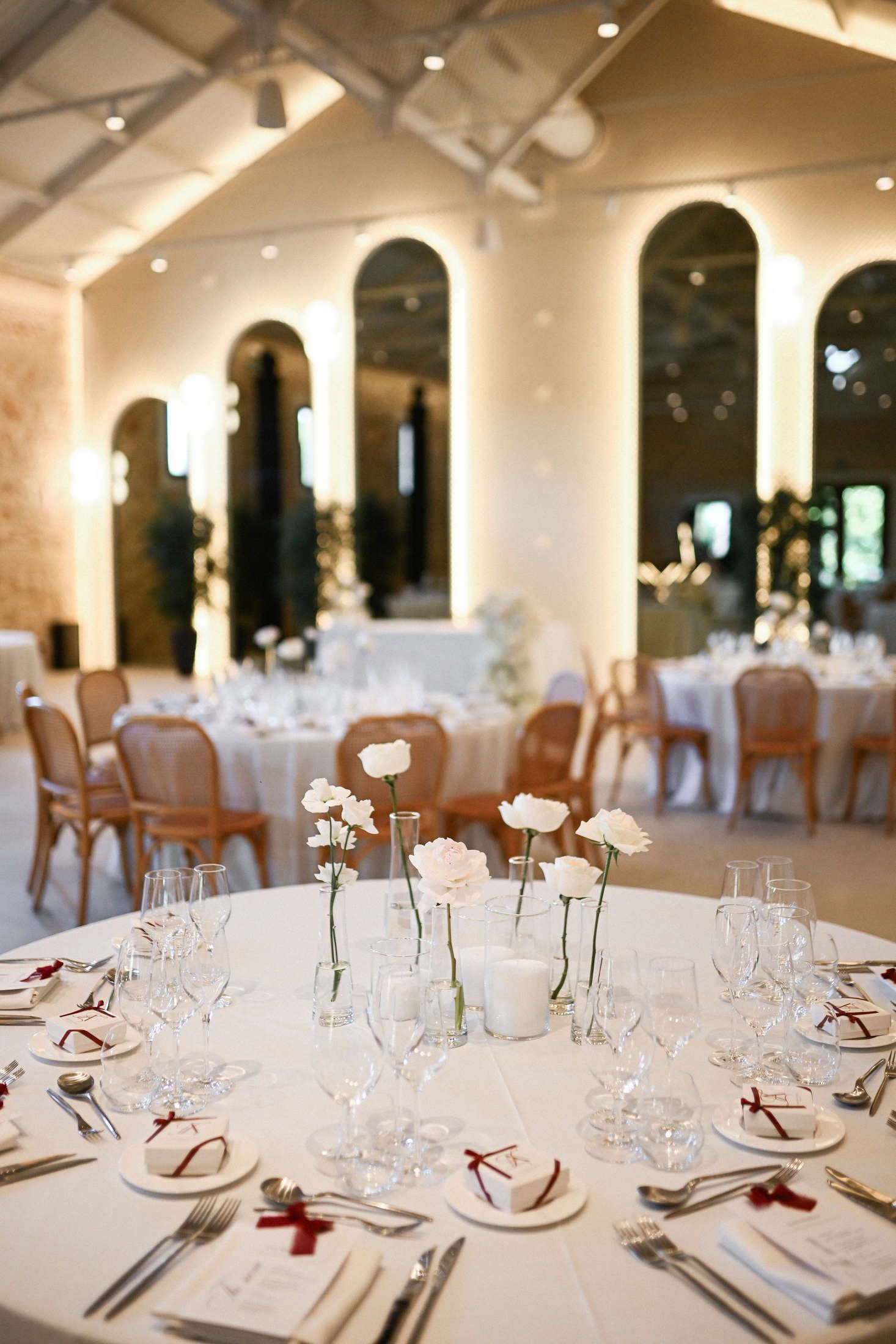 Elegant wedding reception table setting with single white roses in glass vases at a destination celebration in Valencia.