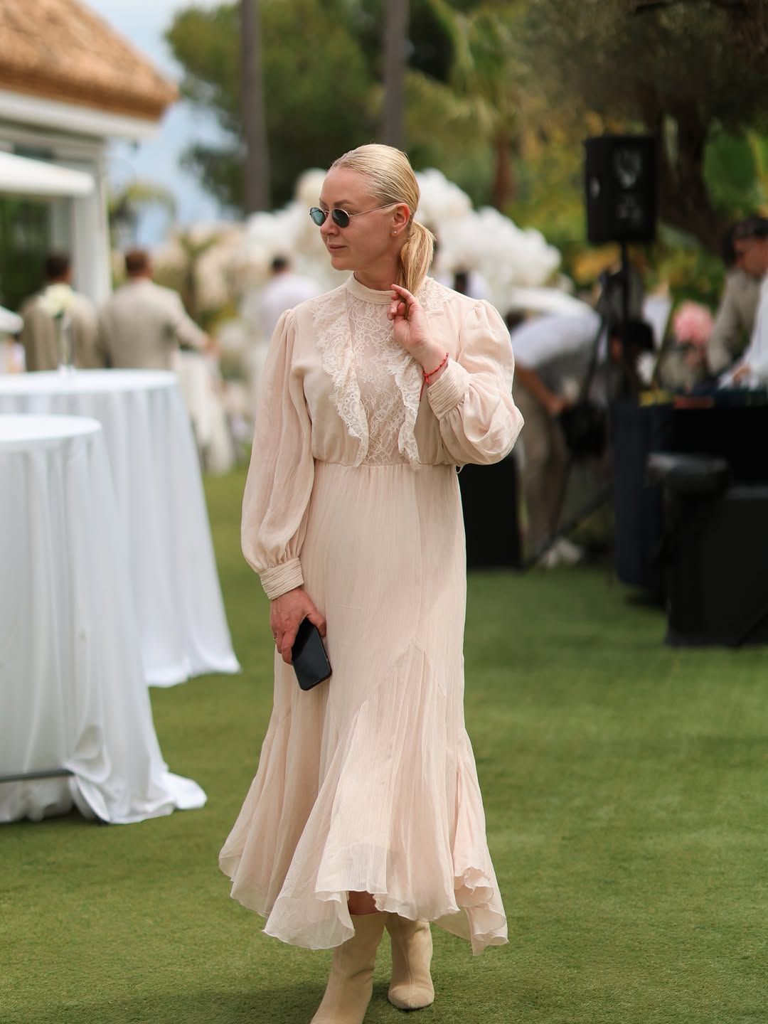 Wedding planner in Alicante, Olga Prudko, coordinates an outdoor event wearing a beige dress and sunglasses on a green lawn.