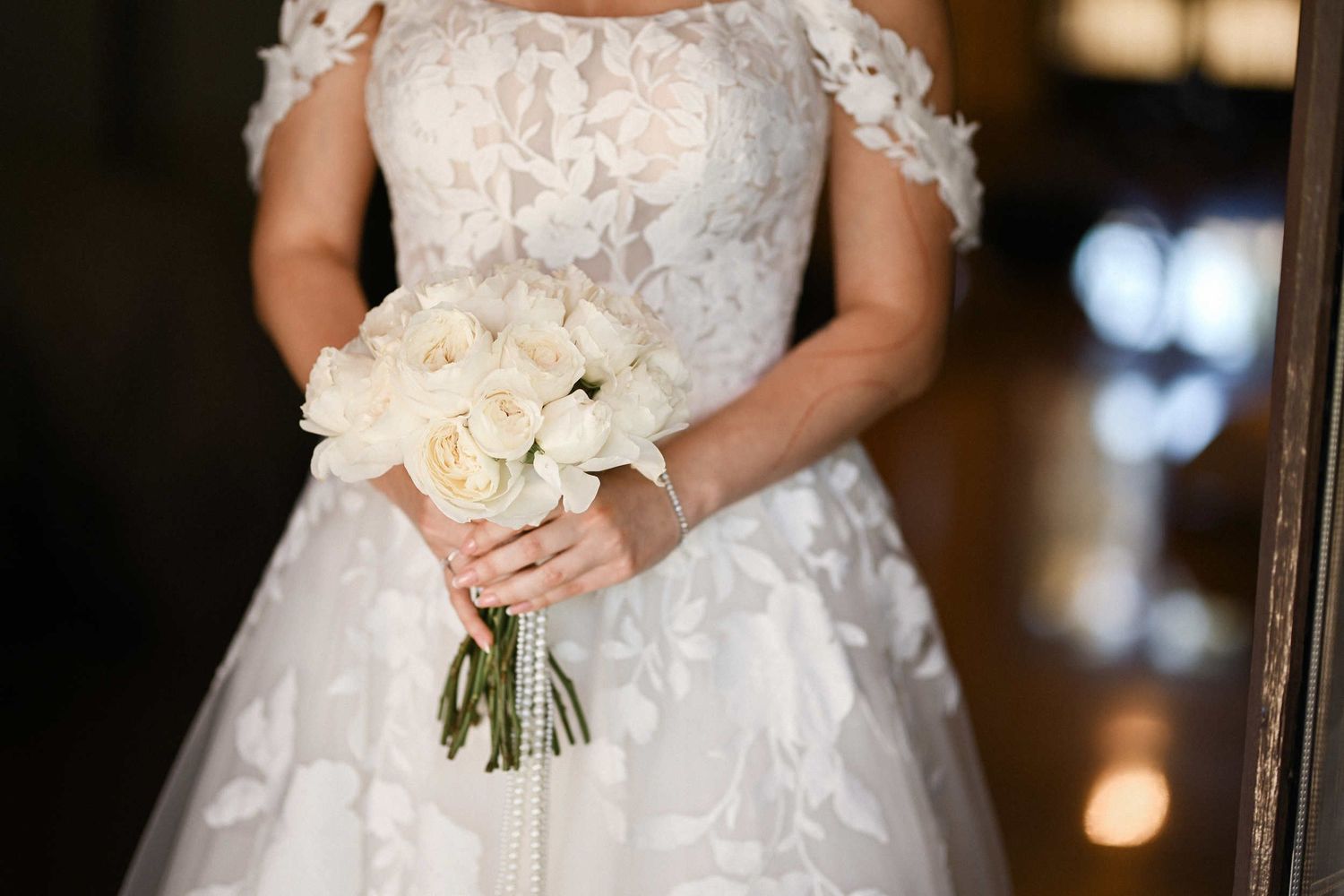 Close-up of a bride in an off-the-shoulder lace dress holding an elegant white rose bouquet at her benidorm wedding.