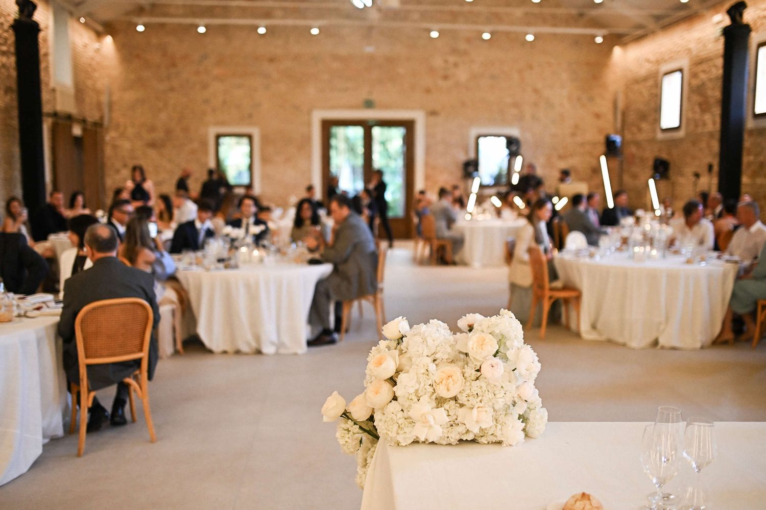 Lush white floral arrangement on the sweetheart table with wedding guests dining in the background at Finca del Canónigo.