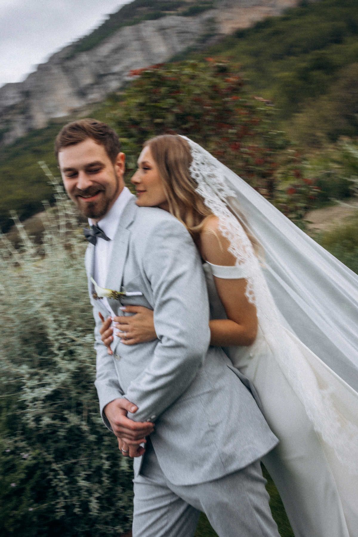 Joyful blurry motion portrait of a bride in a lace veil hugging her groom from behind at a Spanish destination wedding.