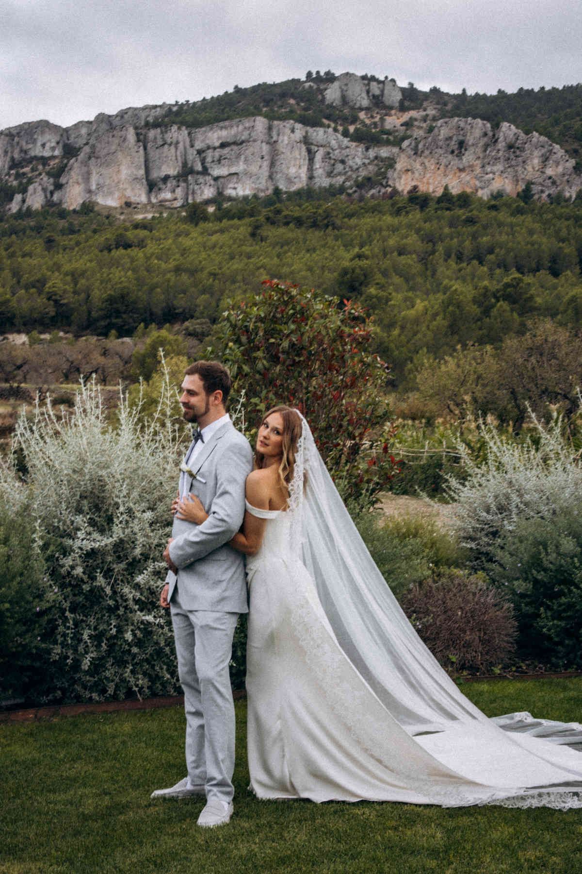 Bride leaning on groom's back with stunning limestone cliffs of the Guadalest Valley in the background at their winery wedding.