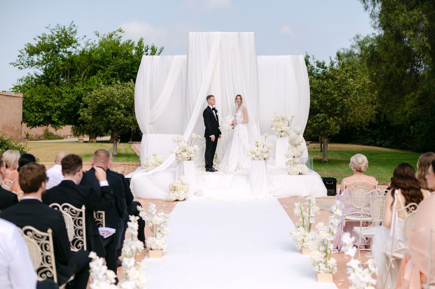 Bride and groom exchanging vows under an elegant white draped altar with floral arrangements at a Valencia wedding.