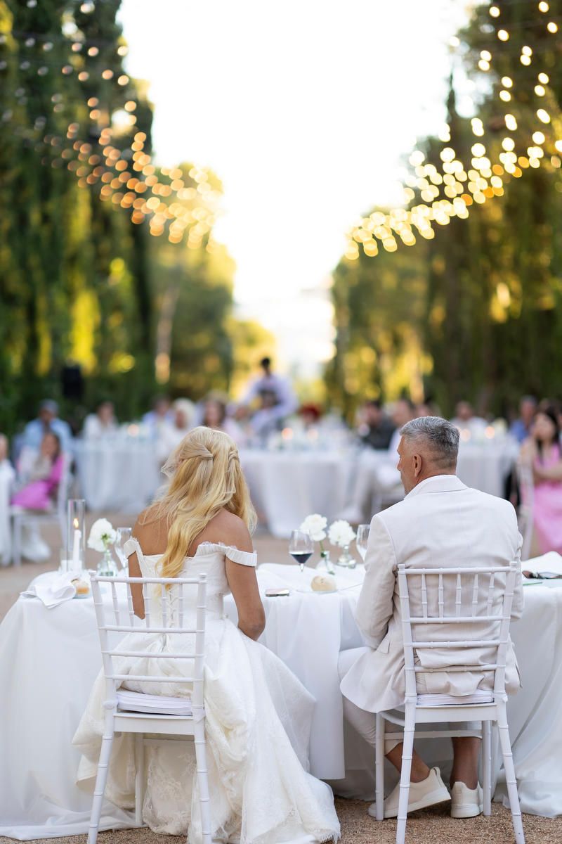 Newlyweds sitting at their sweetheart table beneath glowing string lights during an evening Costa Blanca wedding reception.