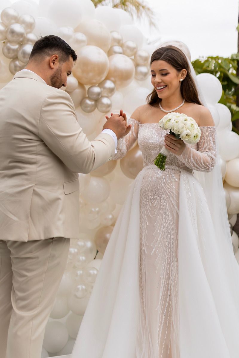 Newlyweds smile and hold hands by a modern balloon display, expertly organized by a top wedding planner in Alicante.