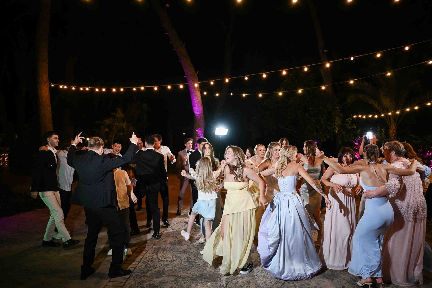 Happy wedding guests and newlyweds dancing at an outdoor nighttime reception under string lights at Finca El Senyoret in Spain.