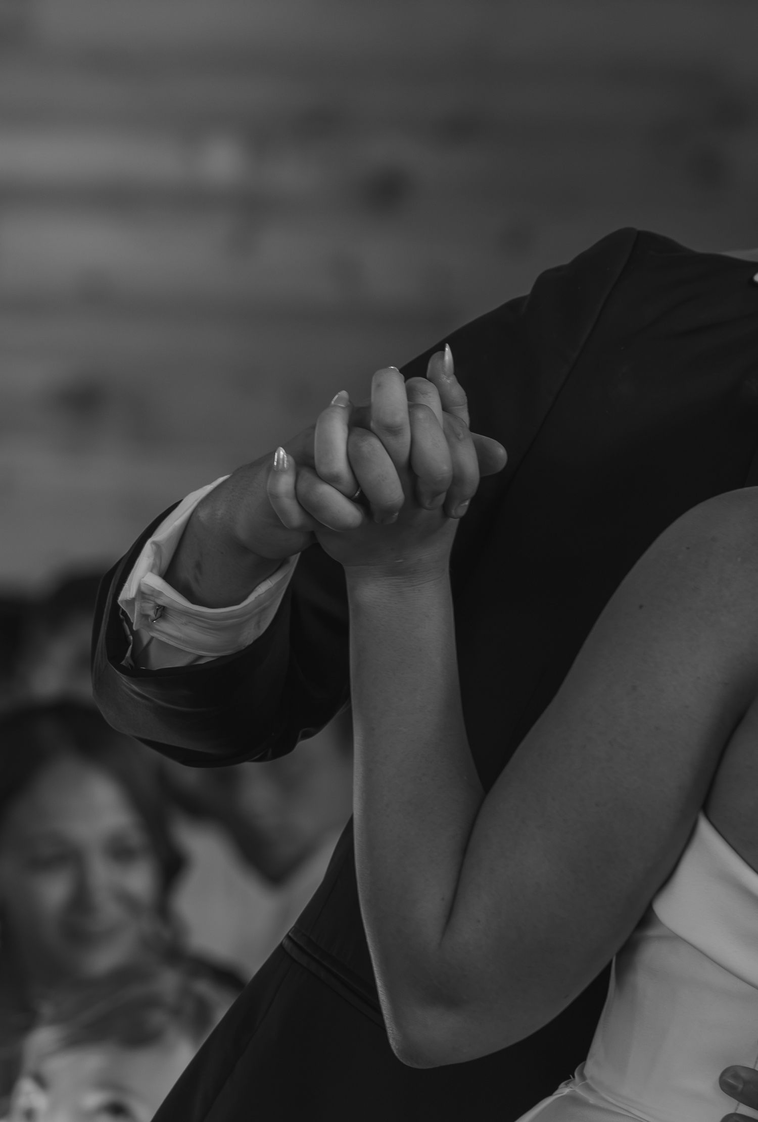 Black and white photo of a couple holding hands during their first dance at a wedding reception.