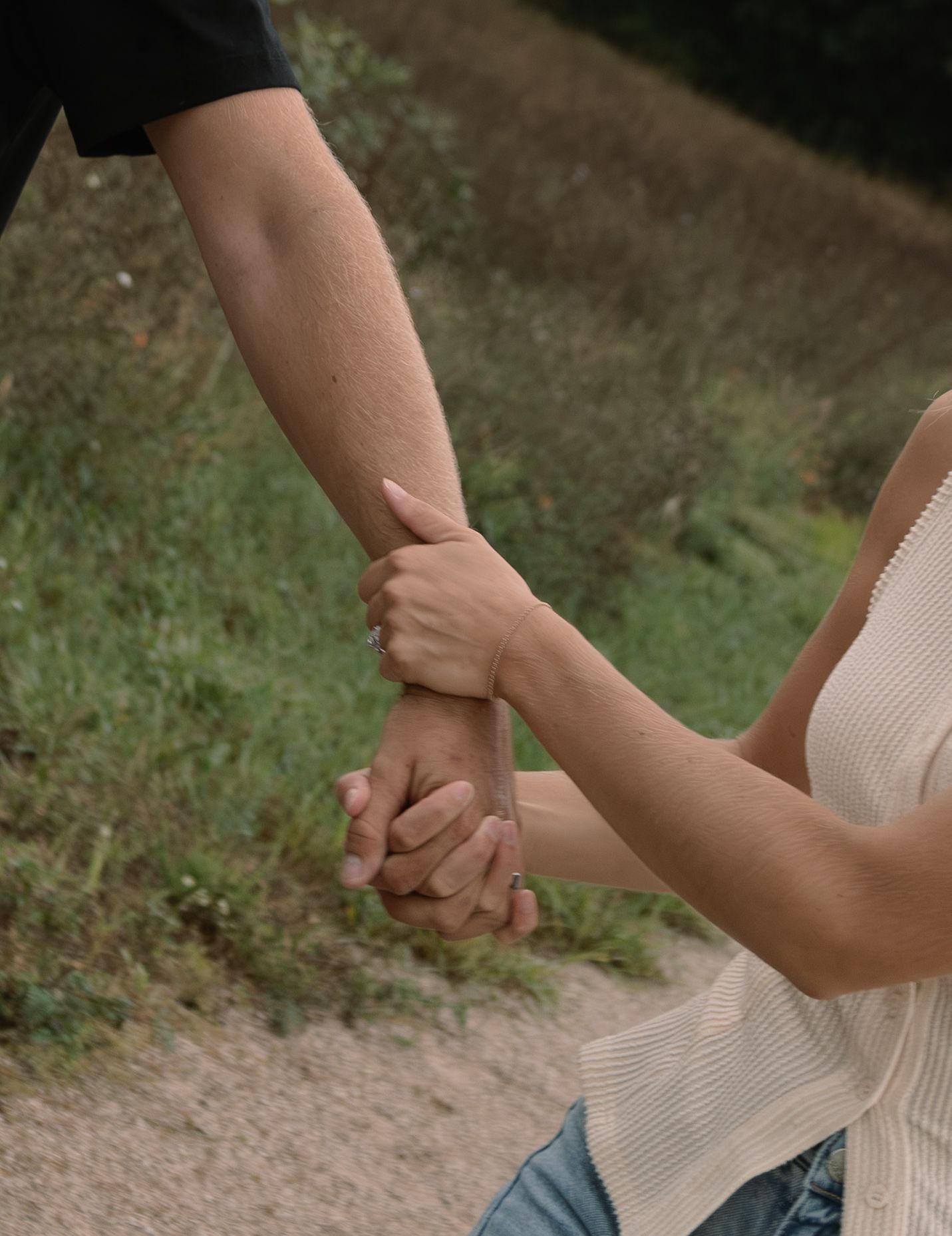 Two people holding hands on a sandy path surrounded by green grass, symbolizing connection and togetherness.